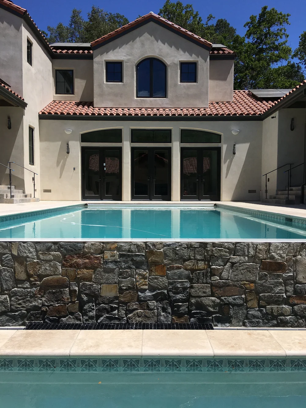  The pool, located between the main house great room and guesthouse, features a waterfall and hand-painted recycled clay tile. 