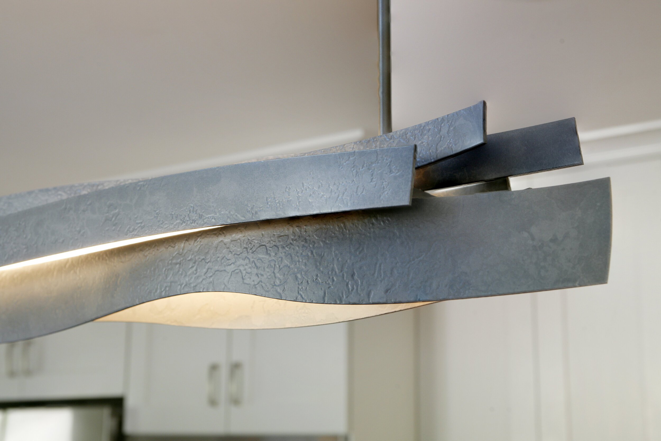 The textured steel light fixture not only illuminates the kitchen island but adds a sculpted element and slightly industrial feel to the space.
