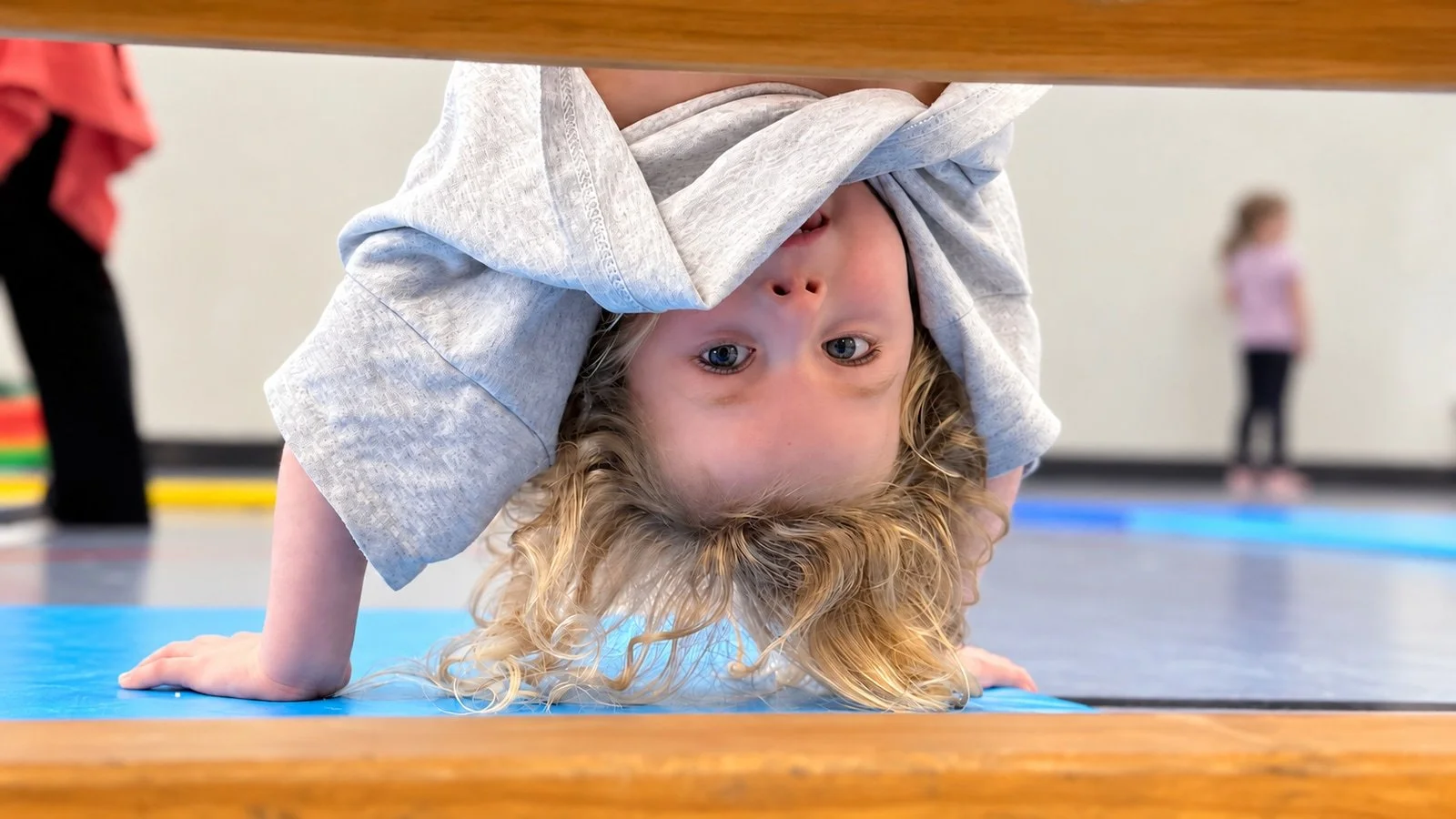 A child looks towards the camera while upside down in the gym; an edited GymLab photograph.