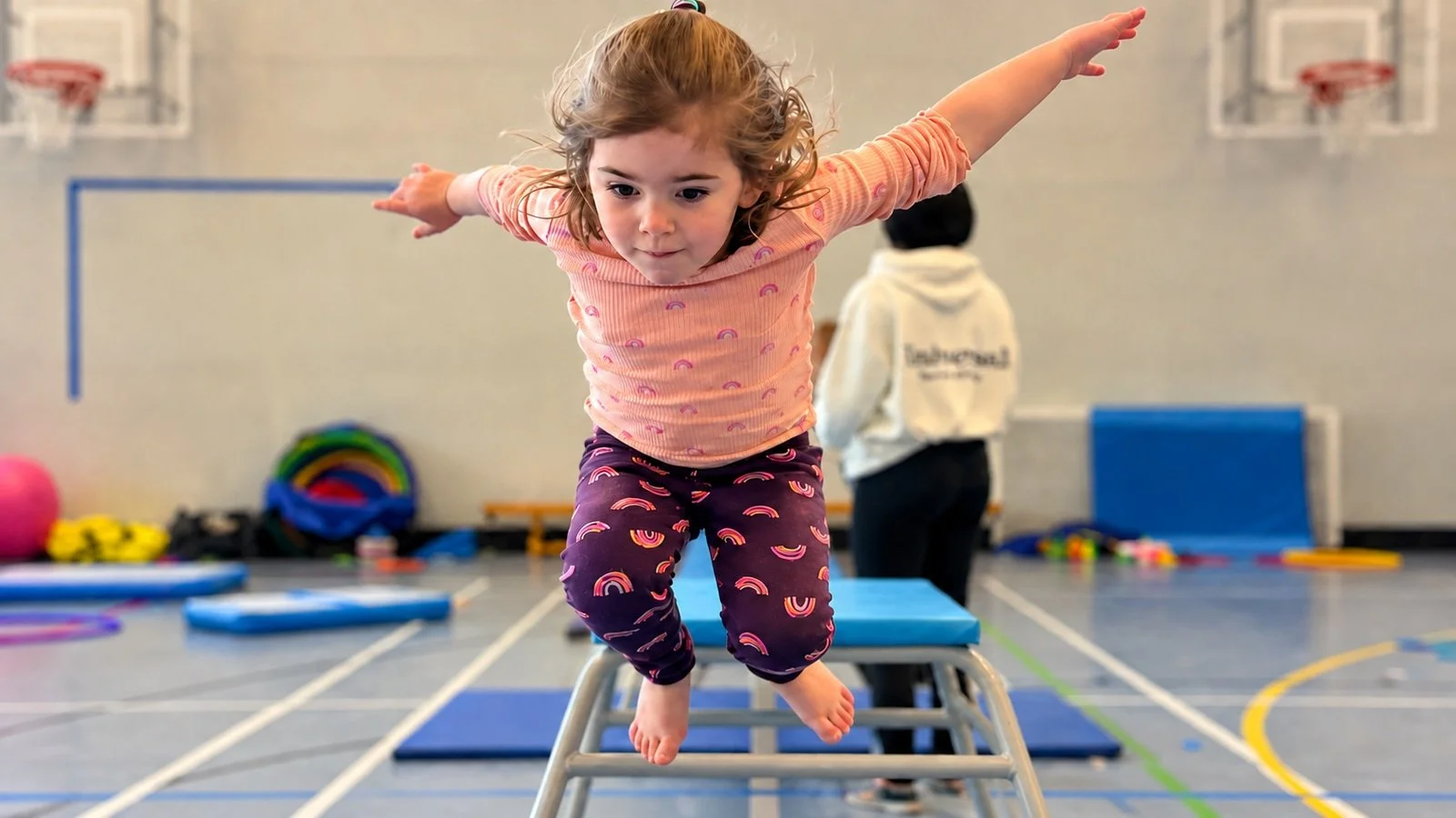 A child jumping with arms outstretched in the sports hall; an edited GymLab photograph.
