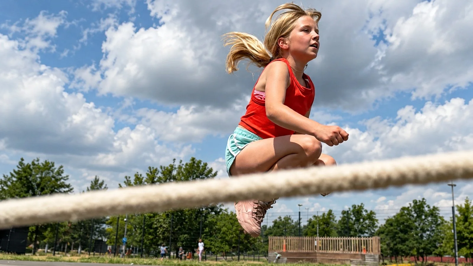 A girl leaping high over a rope outdoors under a bright sky; an edited GymLab Camps photograph.