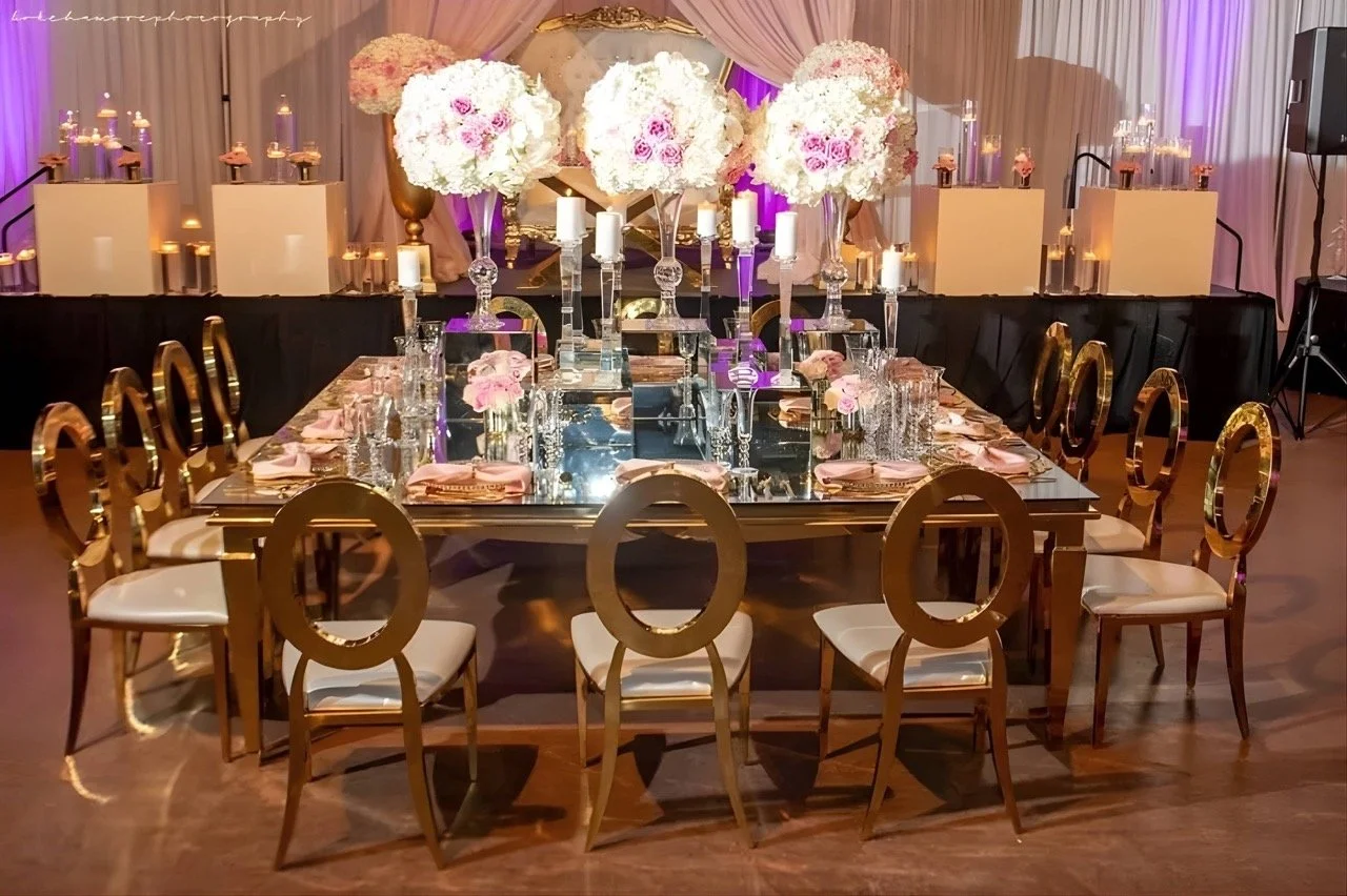 Luxury wedding reception table styled with gold chairs, mirrored surfaces, candles, and elevated floral centerpieces.