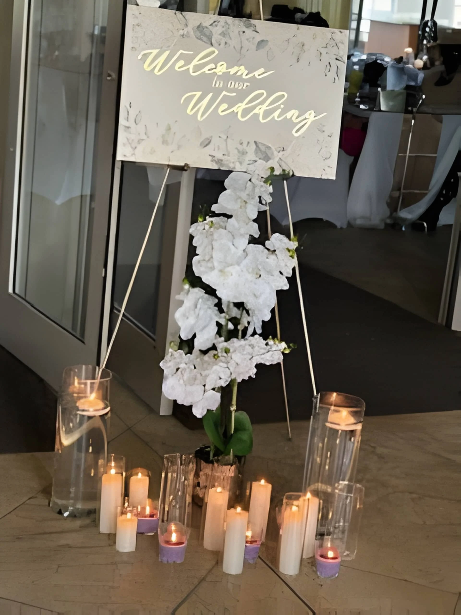 Wedding welcome sign styled indoors with white florals and candles arranged at the base.