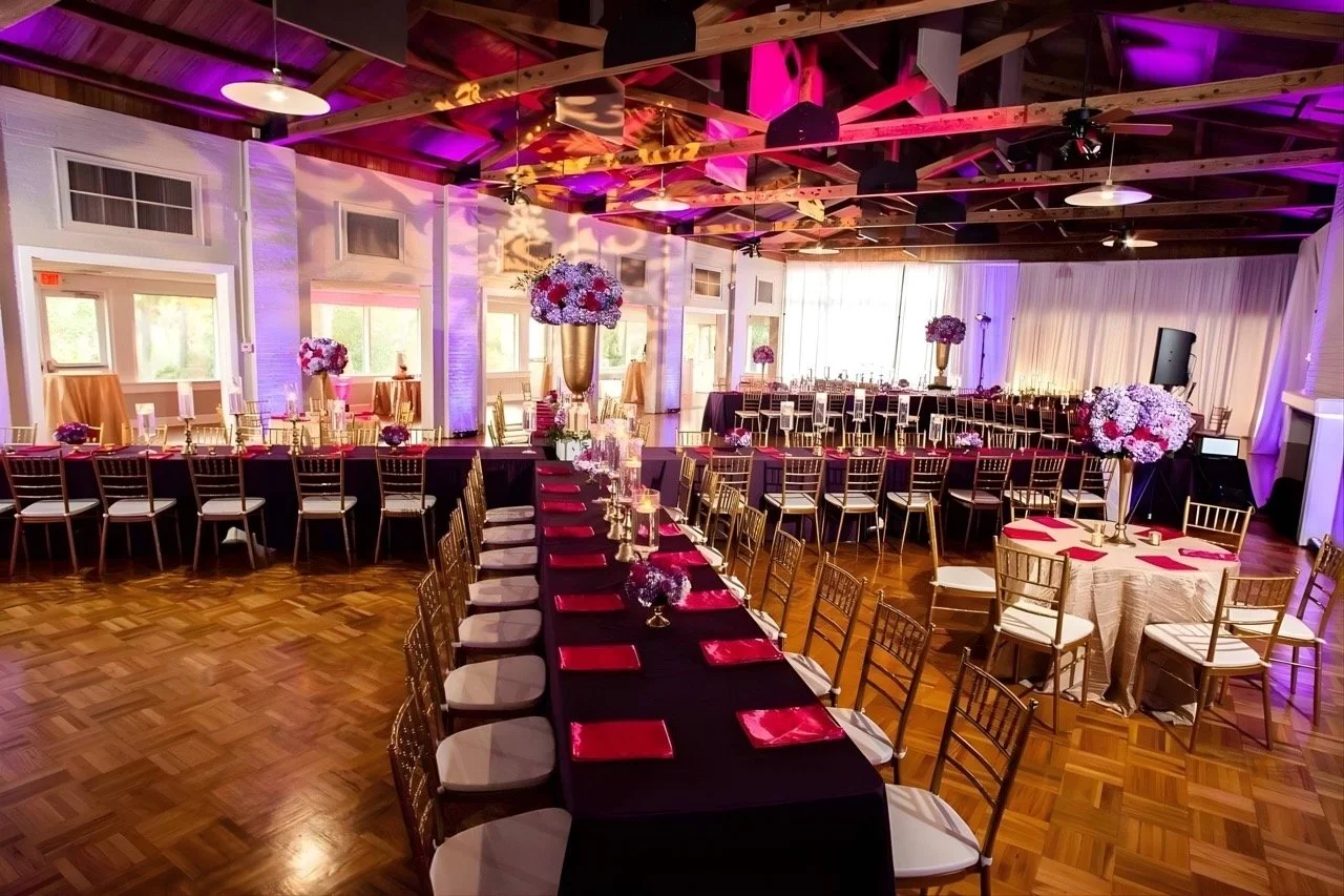 Elegant wedding reception with long banquet tables, gold chairs, floral centerpieces, and ambient uplighting.