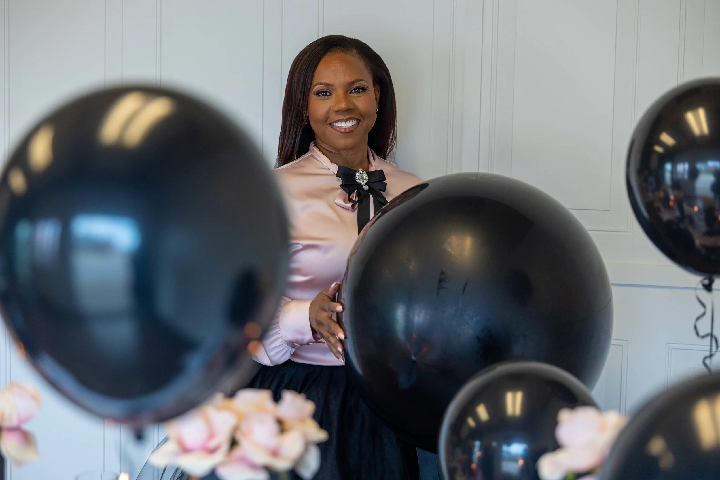 Event stylist standing among black balloons and floral décor in an elegant holiday setup.