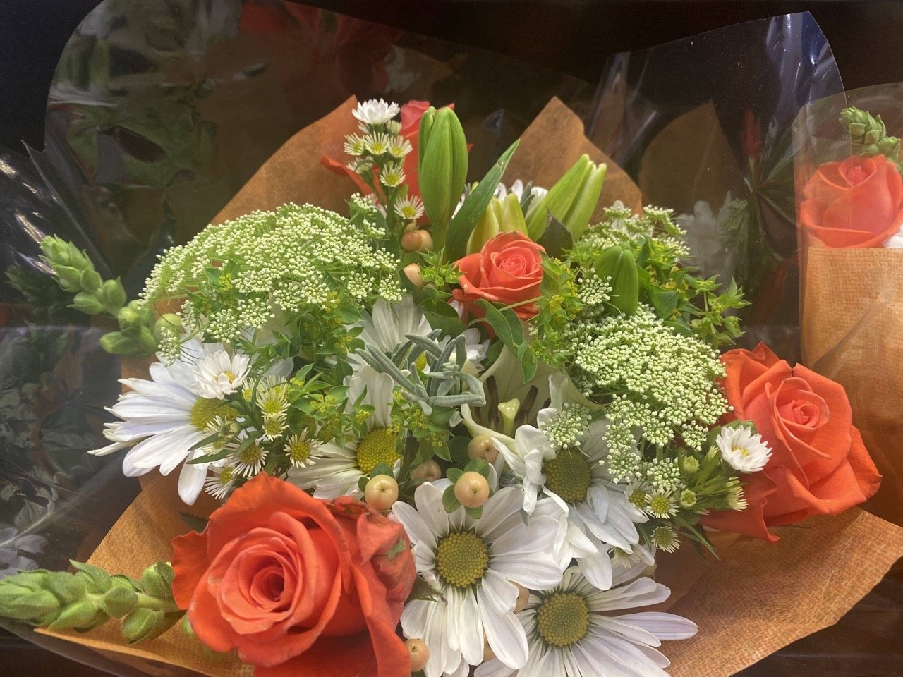 Floral bouquet with white daisies, orange roses, berries, and greenery arranged for an event display