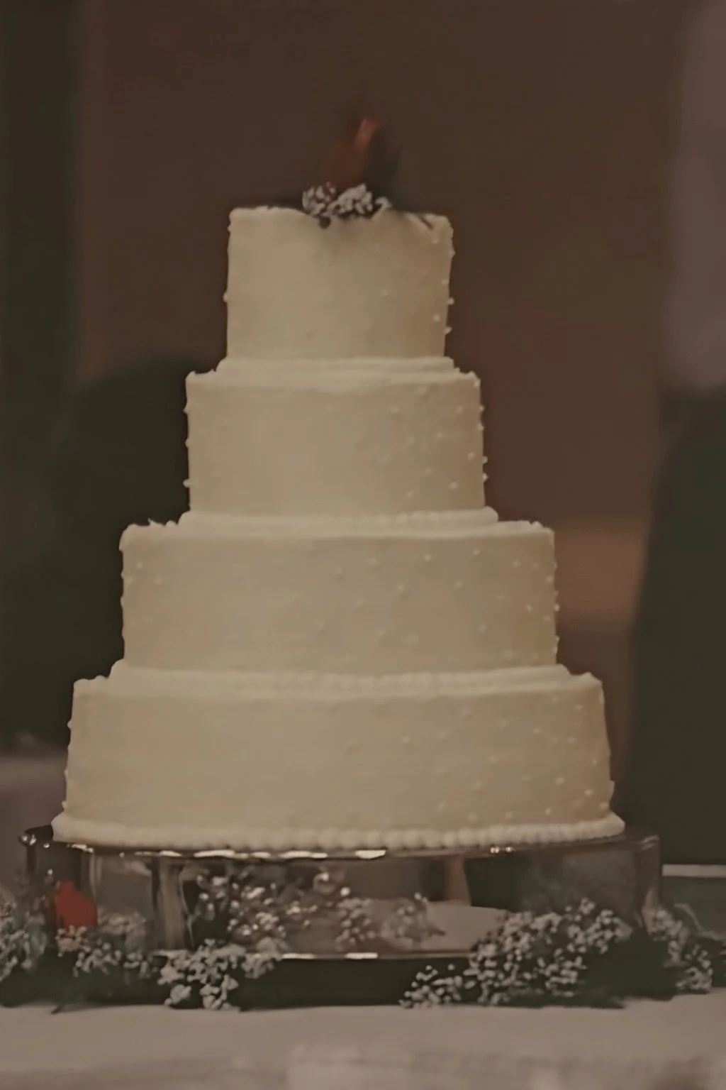 Classic multi-tier white wedding cake with subtle textured detailing, displayed on a formal cake stand.