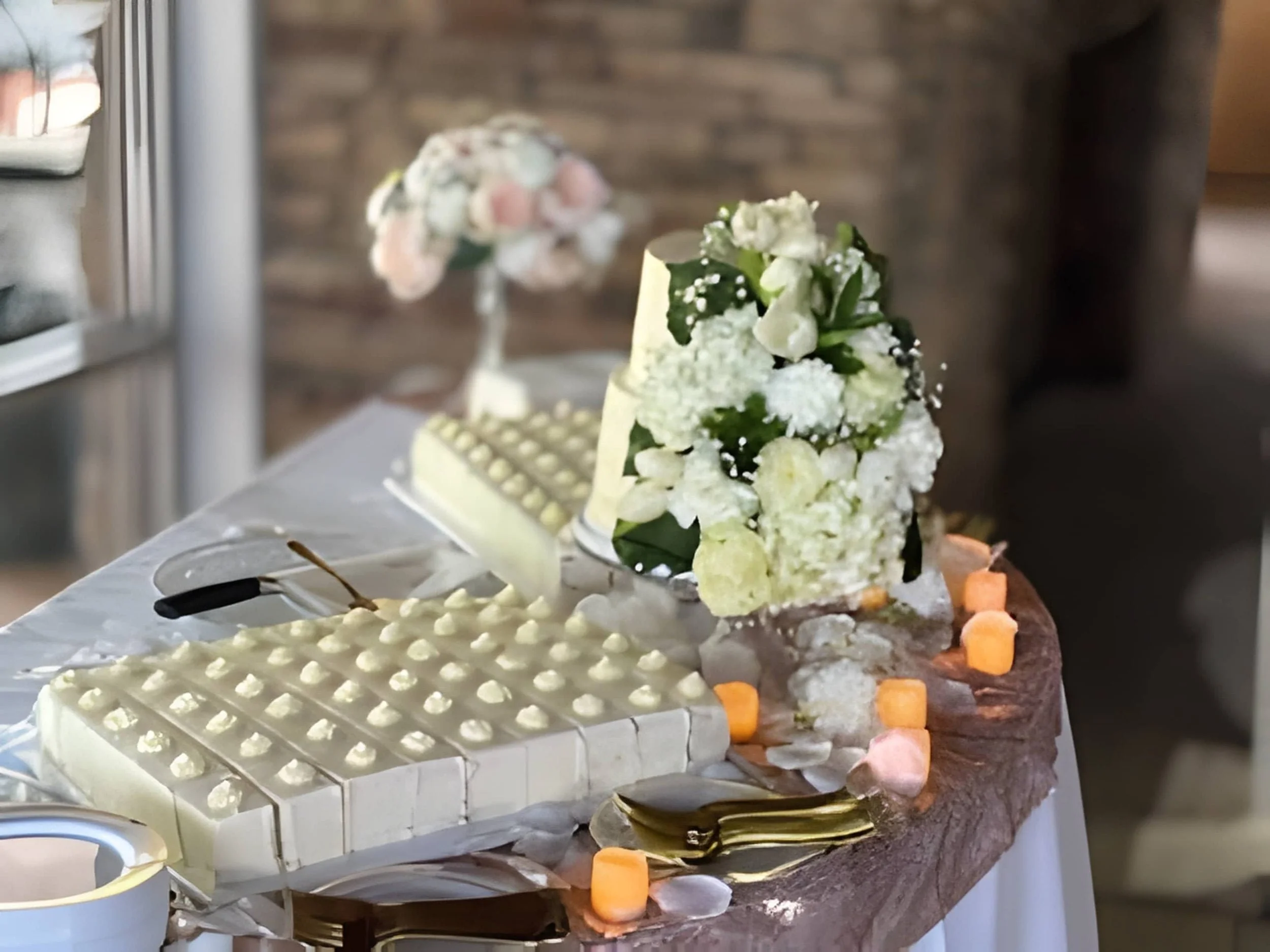 Tiered white wedding cake displayed on a styled table with florals, candles, and serving details.