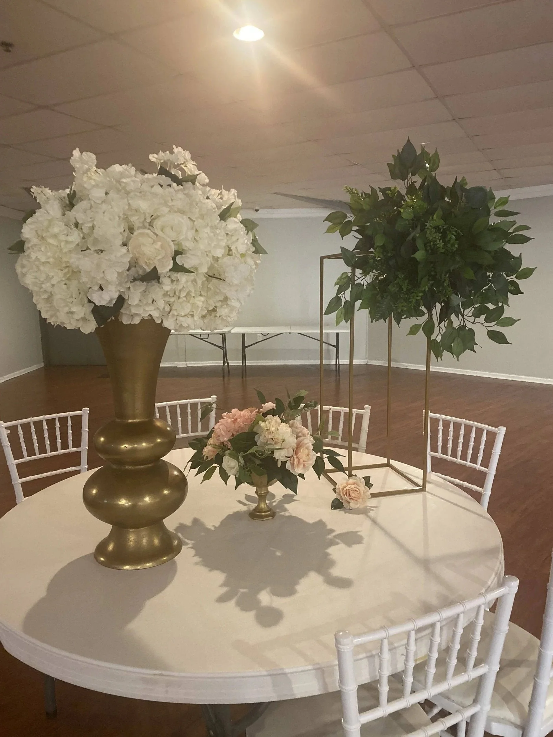 Tall gold vase centerpiece with white florals and greenery on a round event table