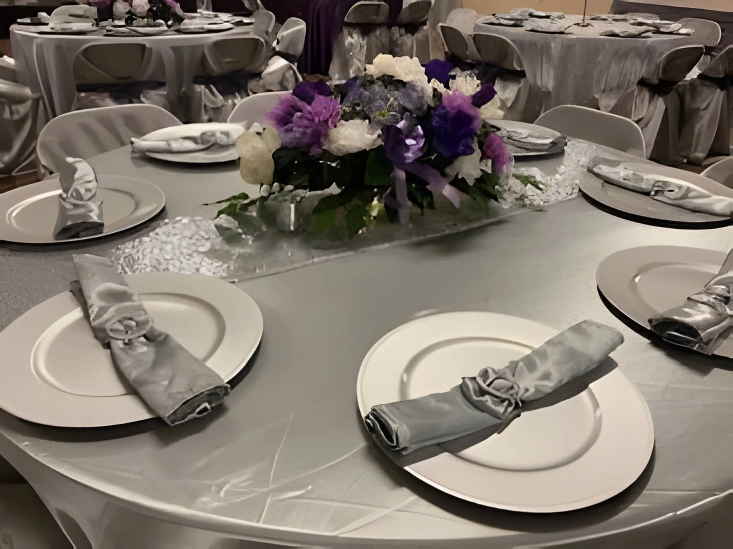 Round reception table set with neutral linens, folded napkins, and a floral centerpiece for a formal wedding event.