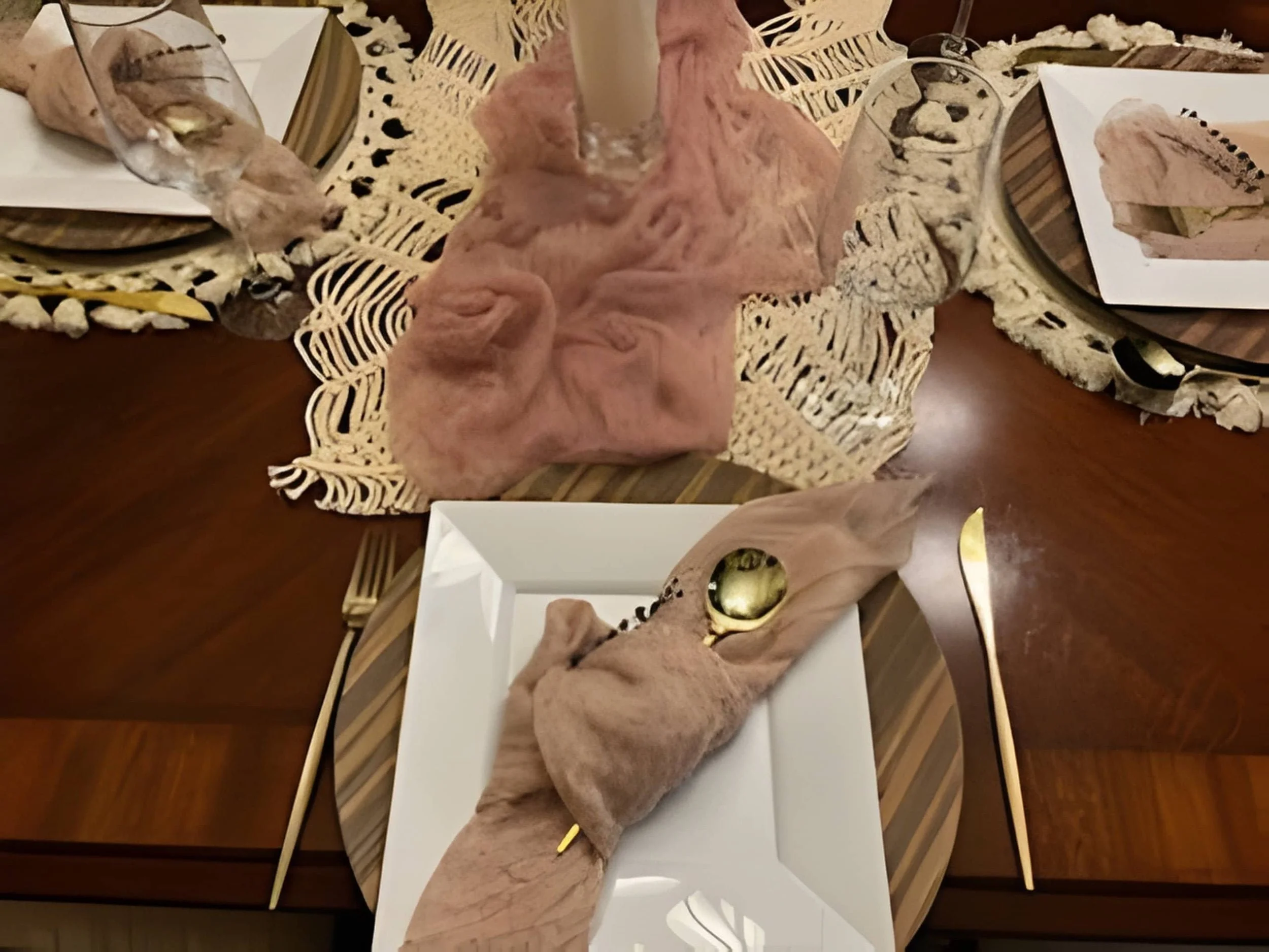 Neutral place setting with layered chargers, blush napkin, gold flatware, and textured runner