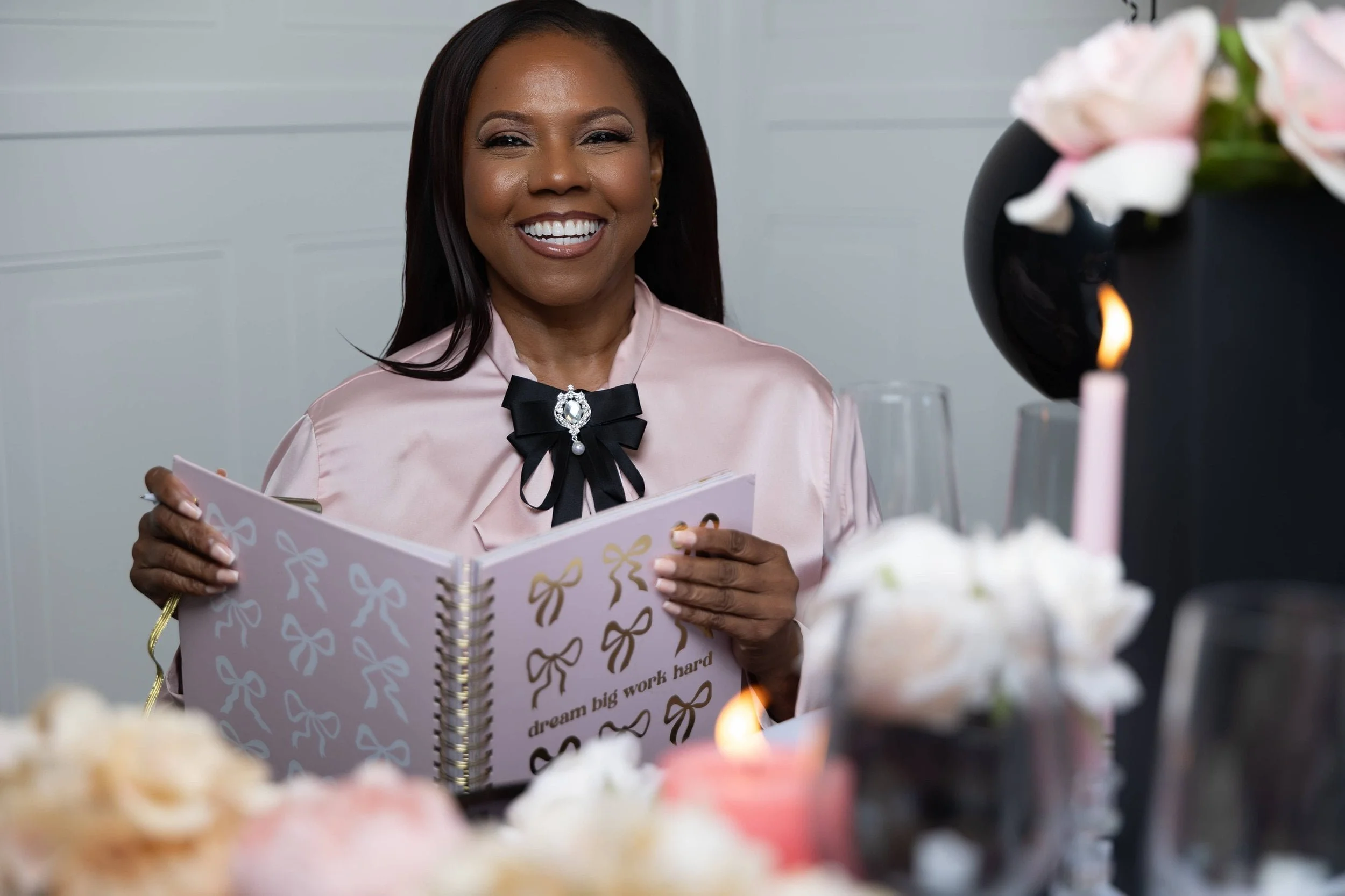 Latonya of Booked Elegant Events holding a notebook at a styled table with candles, and florals.