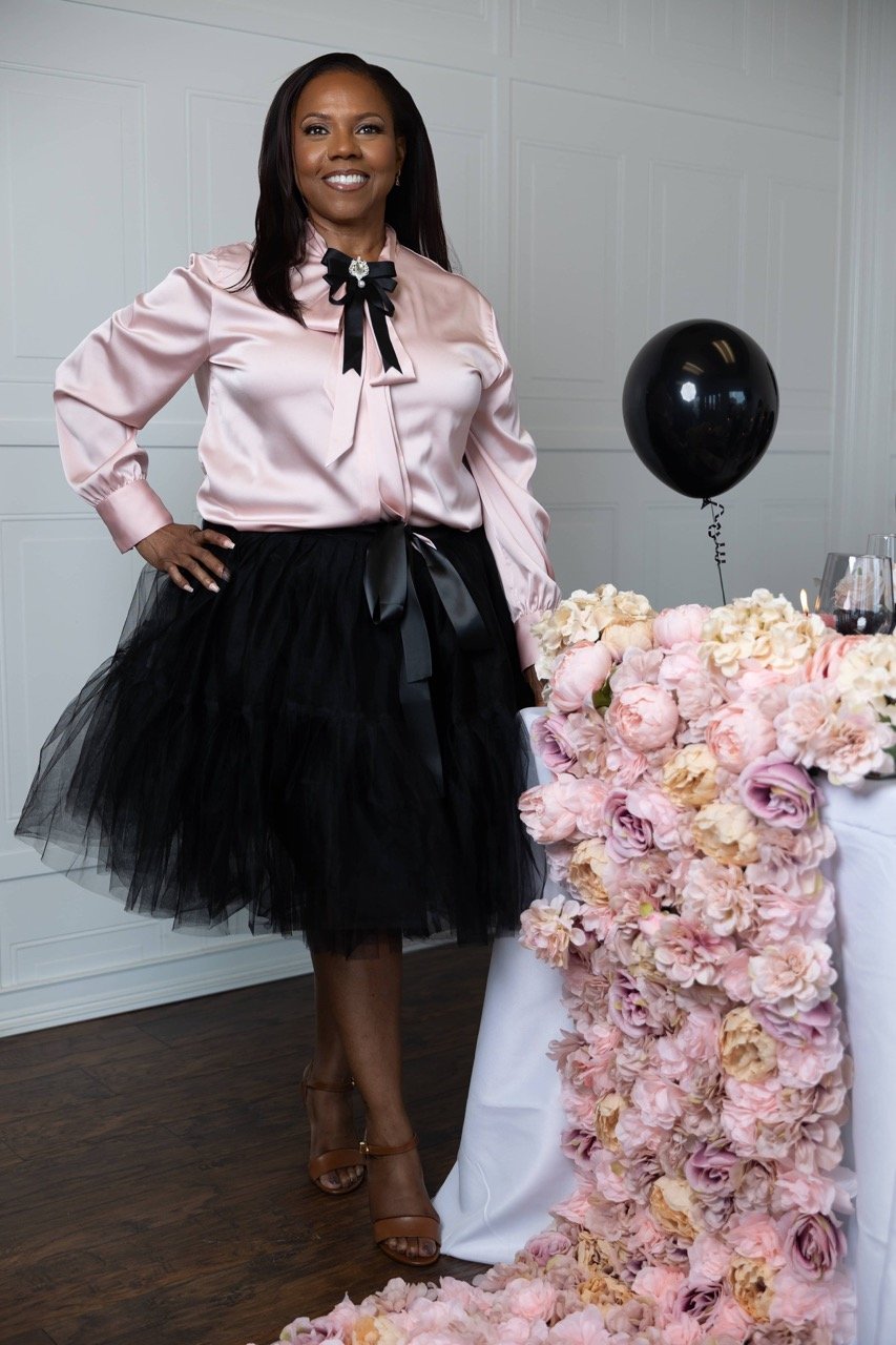 Latonya, owner of Booked Elegant Evens standing beside a table styled with blush floral arrangements and black balloon décor in an indoor studio setting