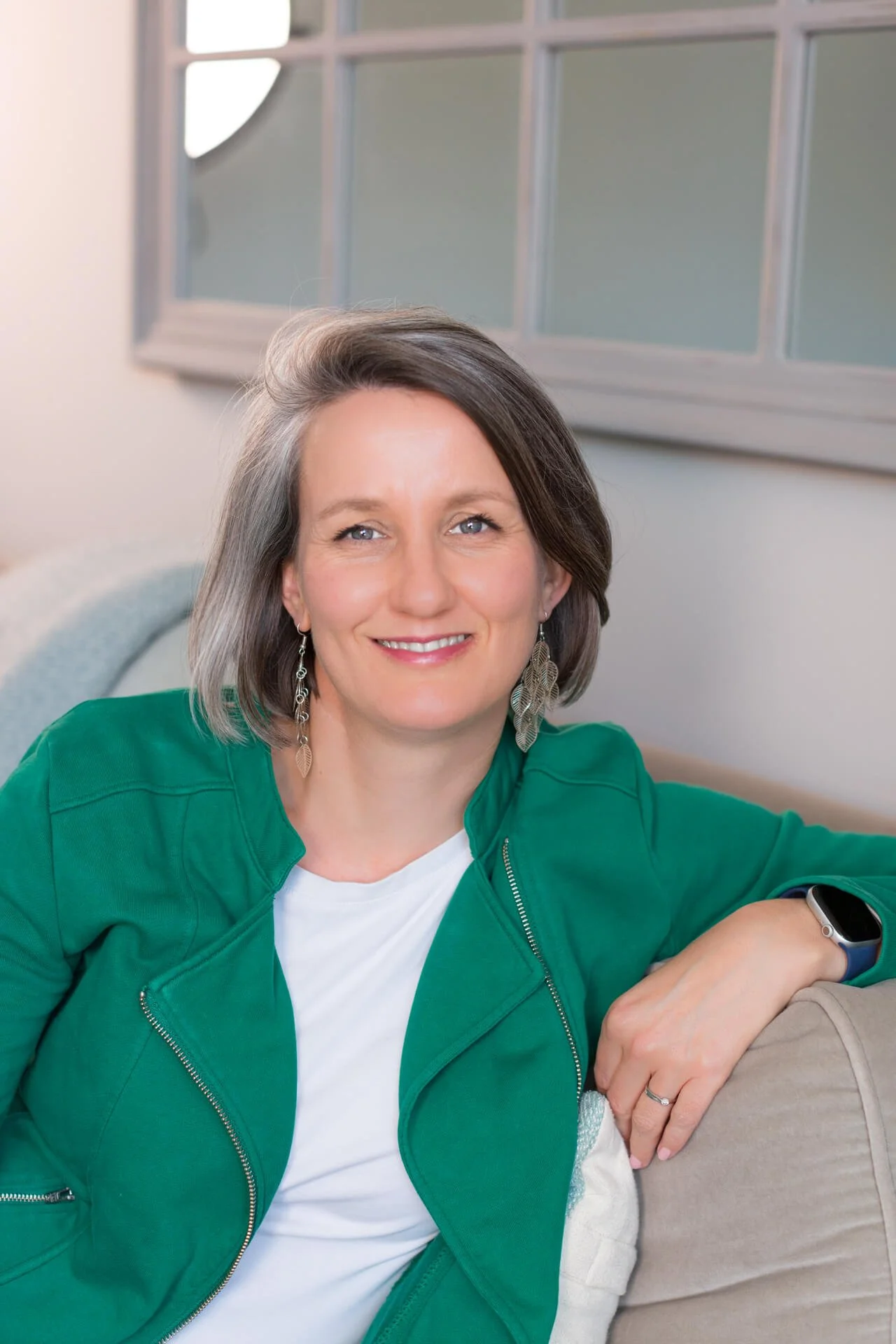 Jo Lofthouse, psychotherapist and EMDR Practitioner, sits on a sofa in a green jacket, smiling