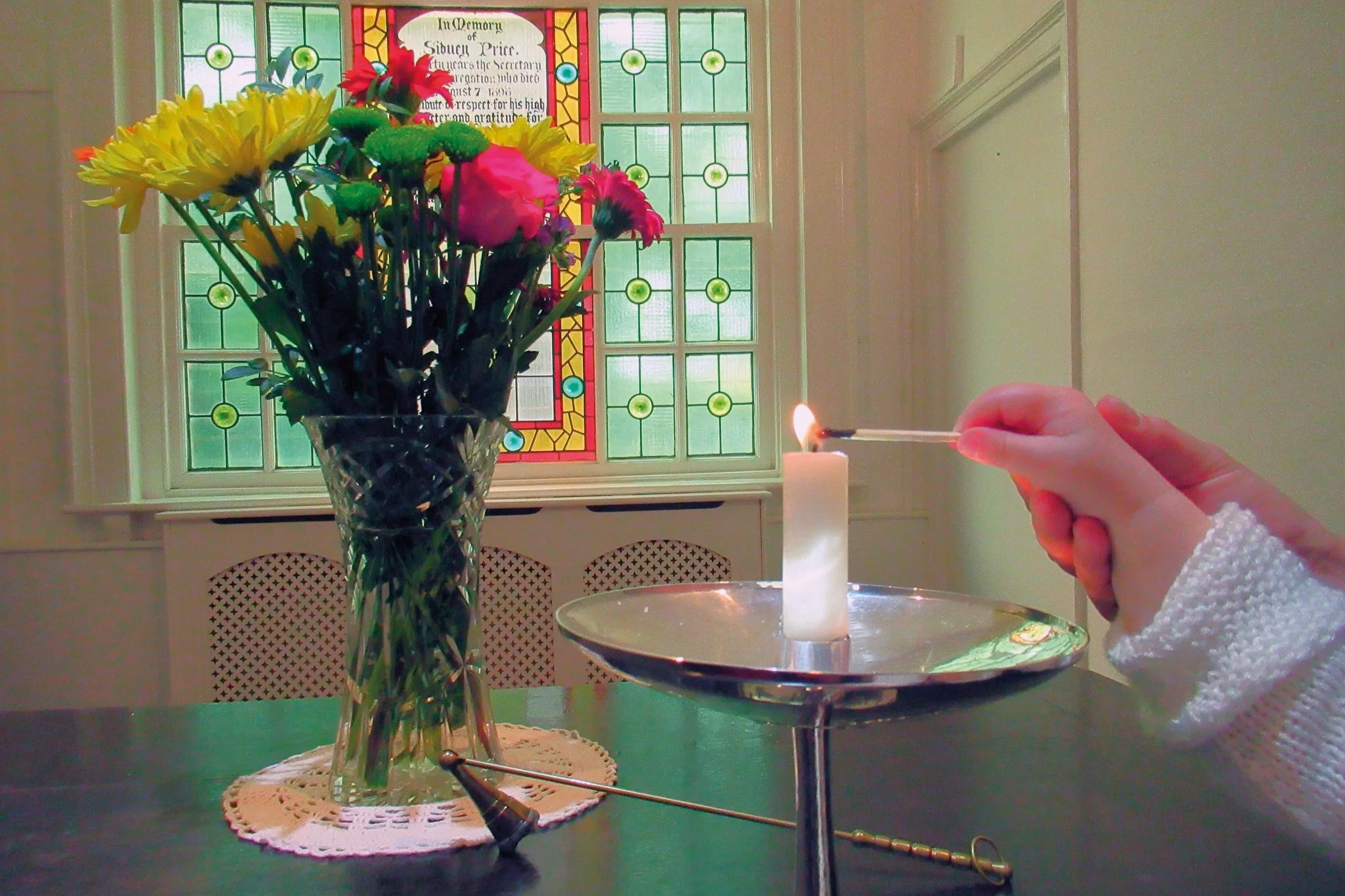 An adults hand gently assists the hand of a child as the light a candle within a chalice.