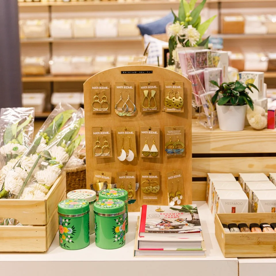 Display of earrings, jewelry, and small gift items on a wooden table in a boutique store.