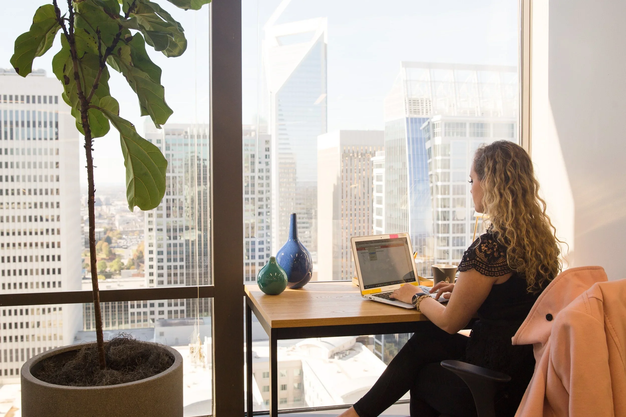 Woman working on a laptop at a desk by a window