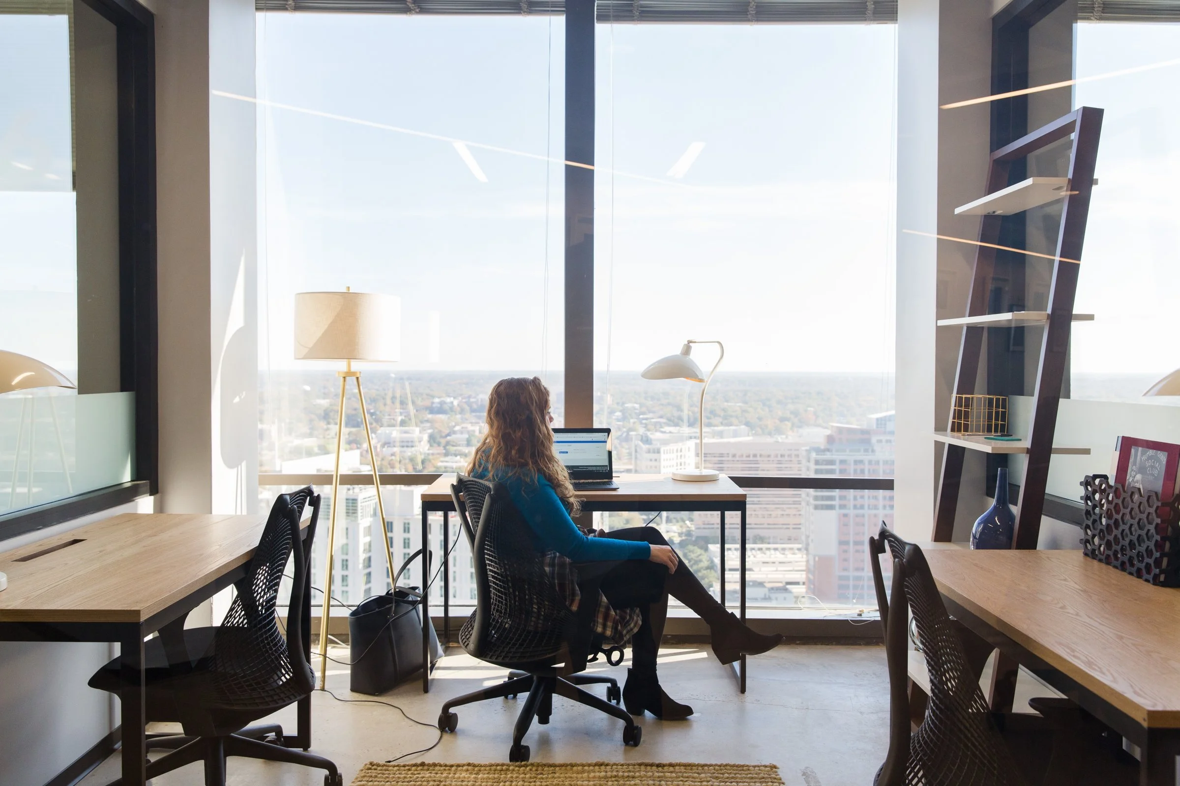 Team member working on a laptop at a window desk in a Charlotte office, with Apple Business Essentials handling device setup and day-to-day admin
