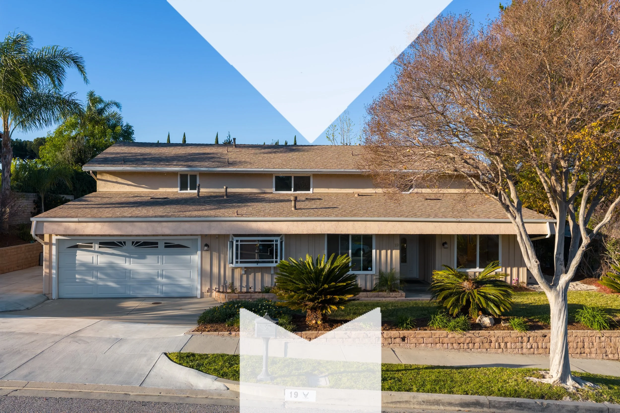 A two-story house with a garage, surrounded by trees and landscaping, under a partly cloudy sky.