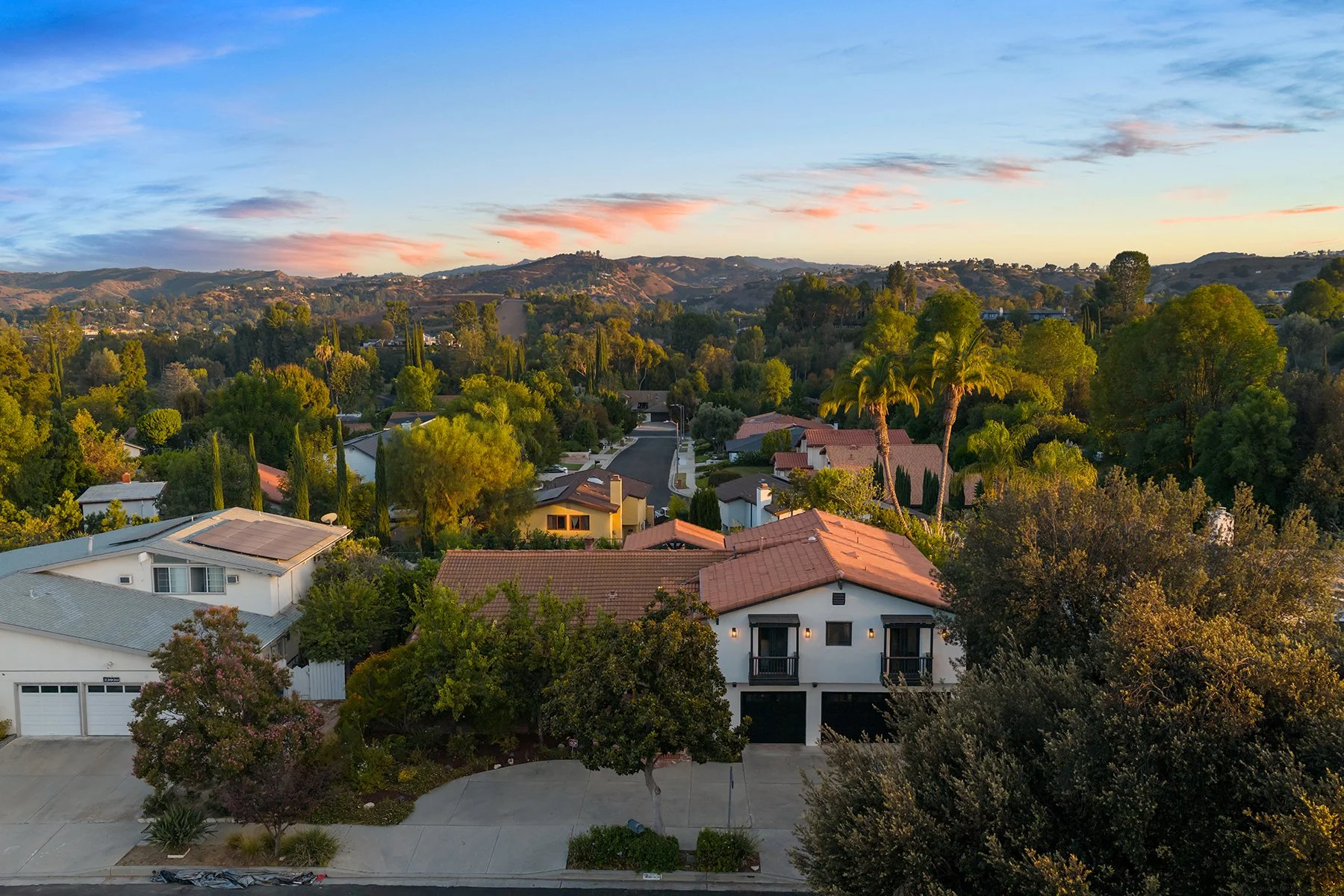 Residential neighborhood with houses, trees, and hills in the background during sunset.