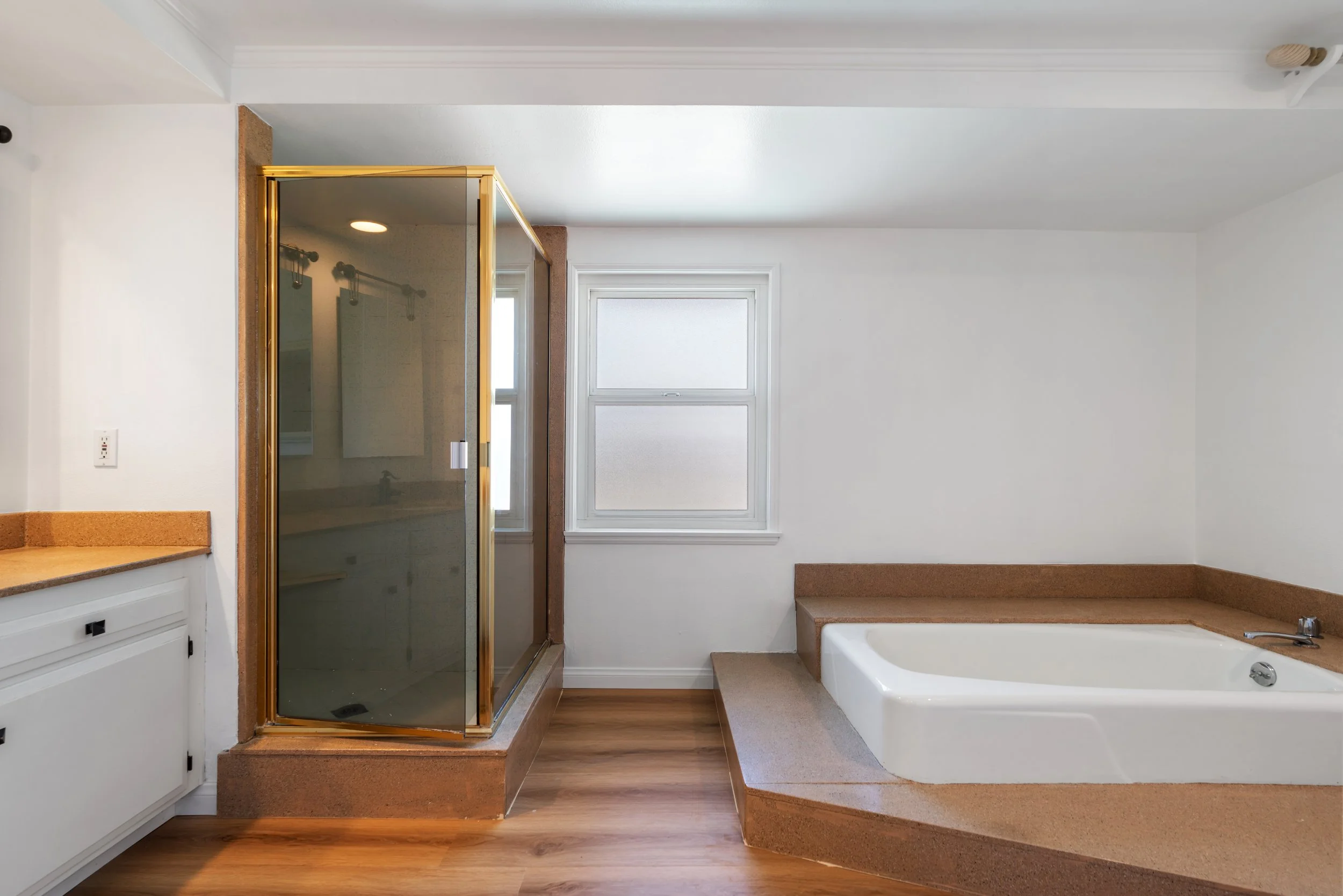 Bathroom with a glass shower enclosure, a window, and a large bathtub with brown surround.