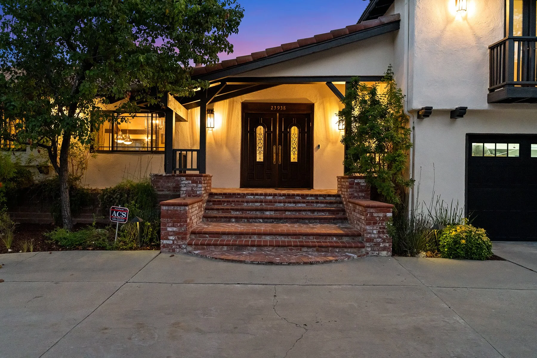 Front entrance of a house with brick stairs, black front door, and warm lighting, surrounded by greenery at dusk. Represented by Phil Missig and the Missig Team.