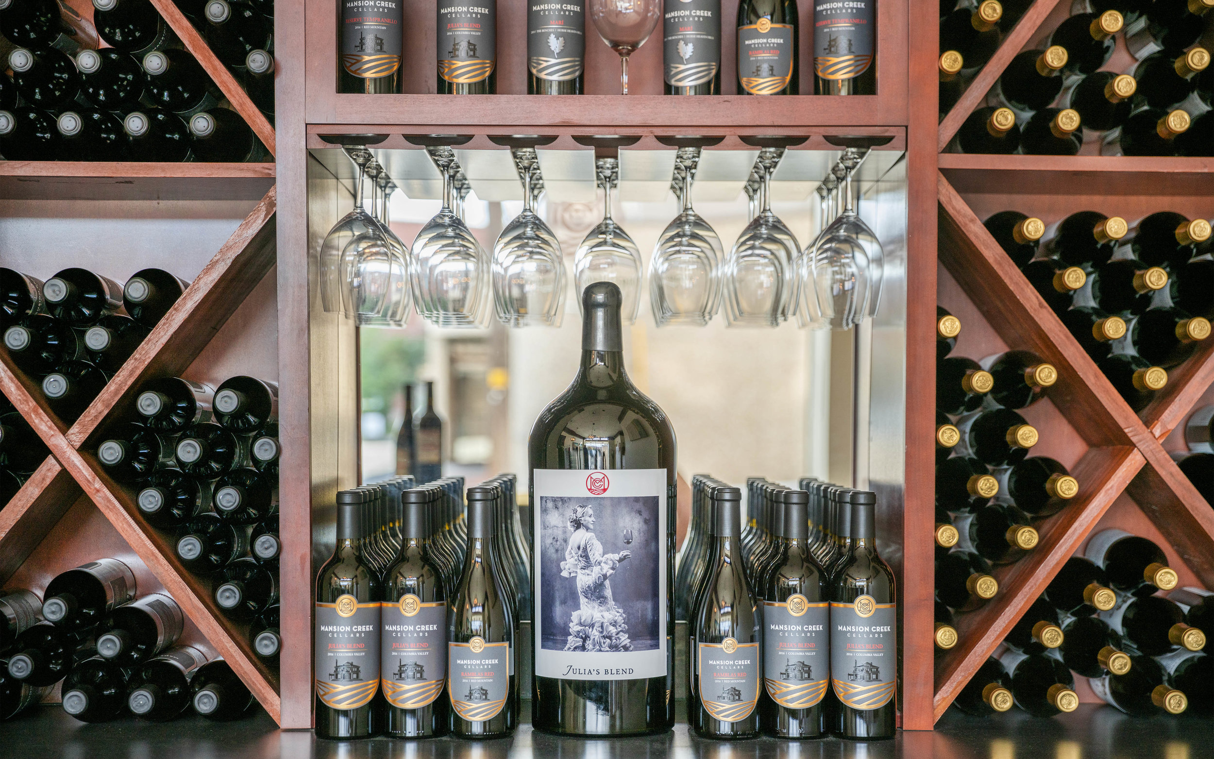 A magnum sized bottle of Mansion Creek Cellars wine, surrounded by bottles and glassware on a shelf in the Walla Walla tasting room.