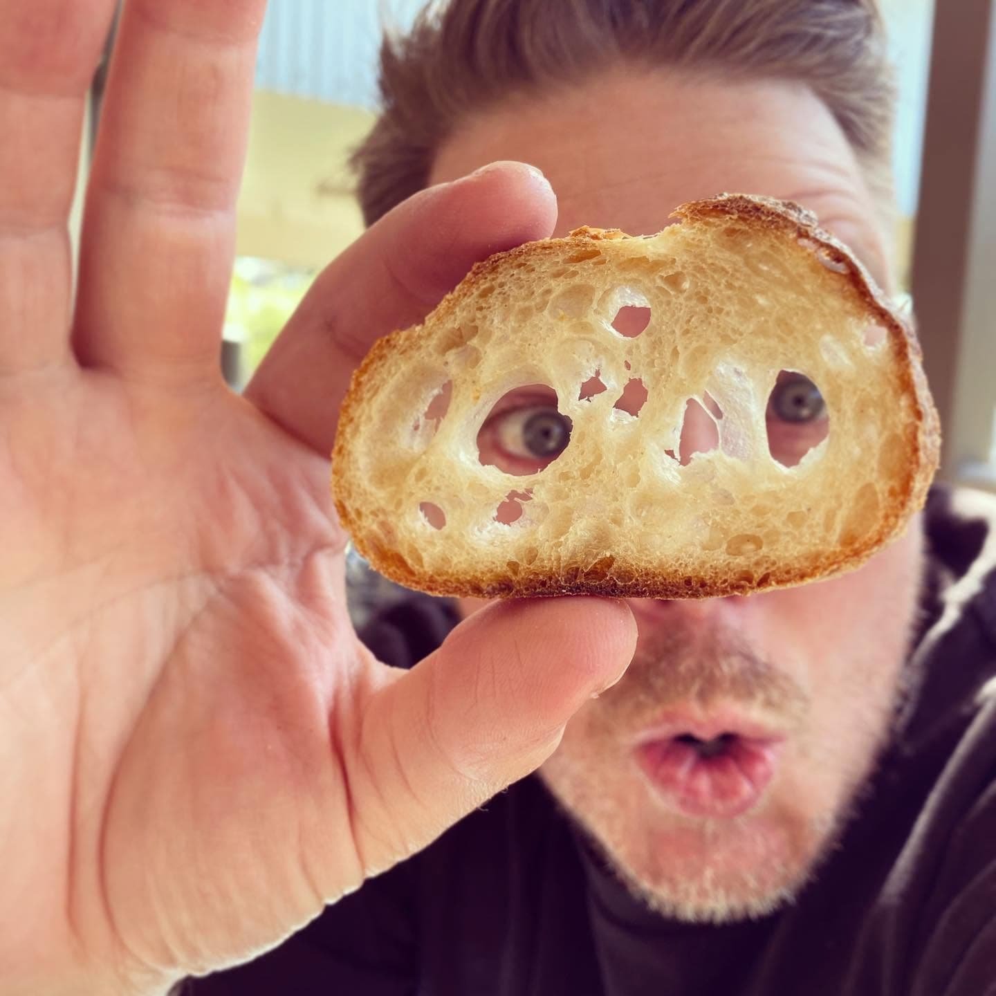 Baker holding a slice of sourdough up to the camera, showing its open crumb.