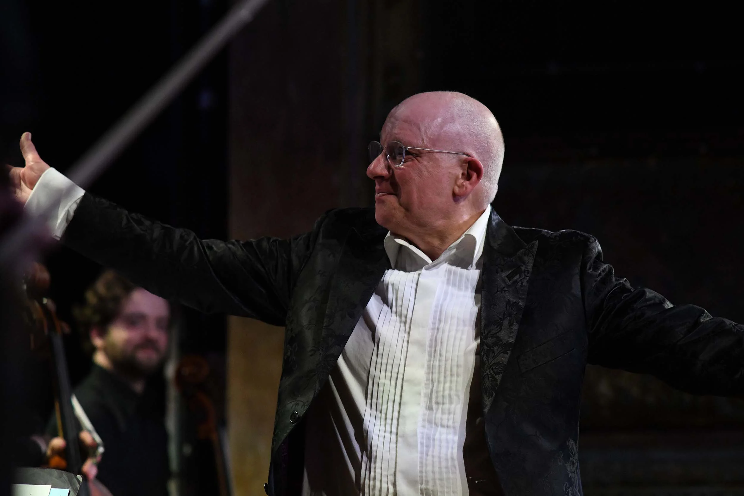 bald-man-glasses-formal-wear-arms-outstretched-orchestra.jpg