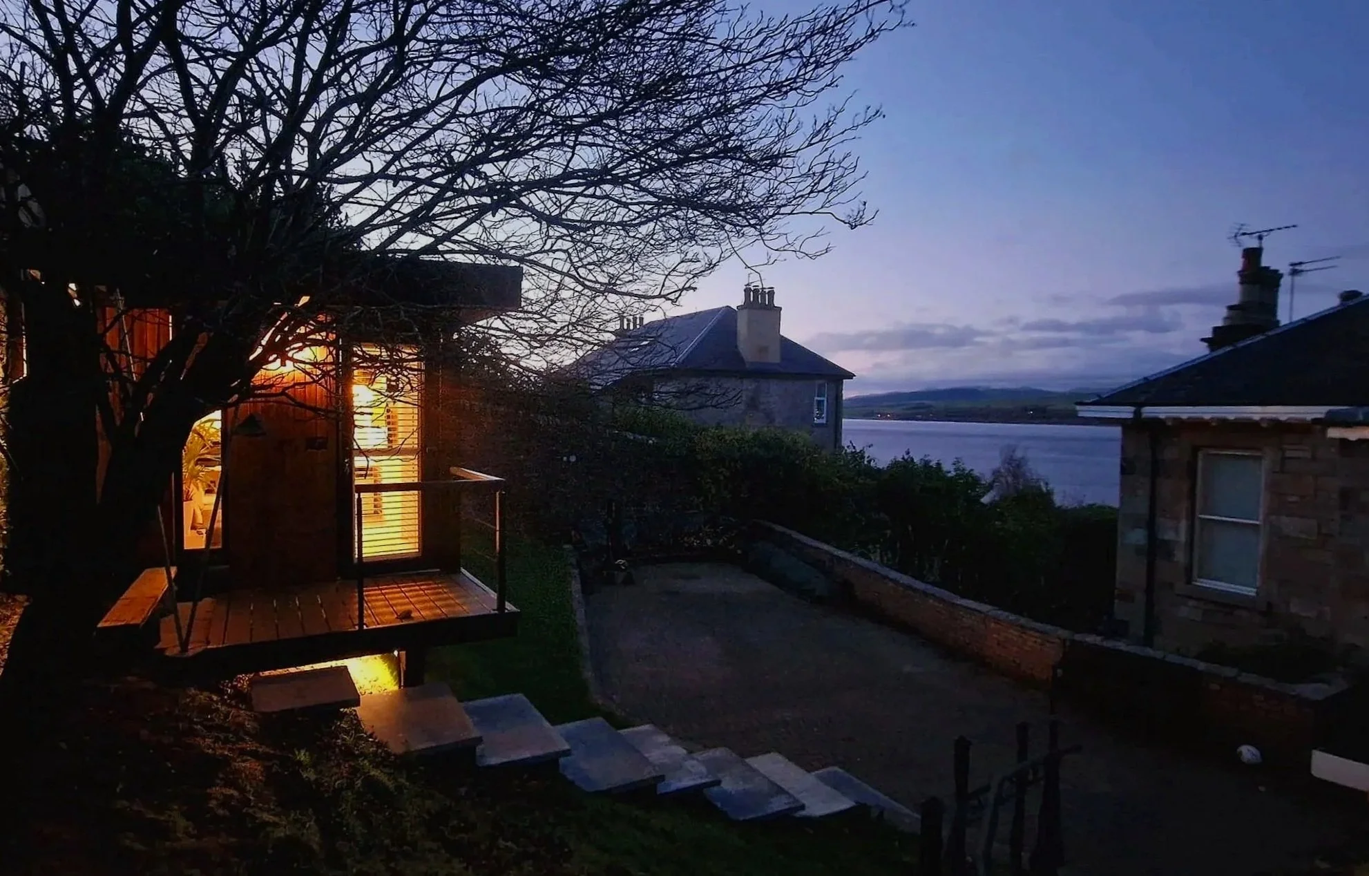 Designer Garden room with tree, a house with a chimney, and a body of water in the distance, early evening sky. Langbank