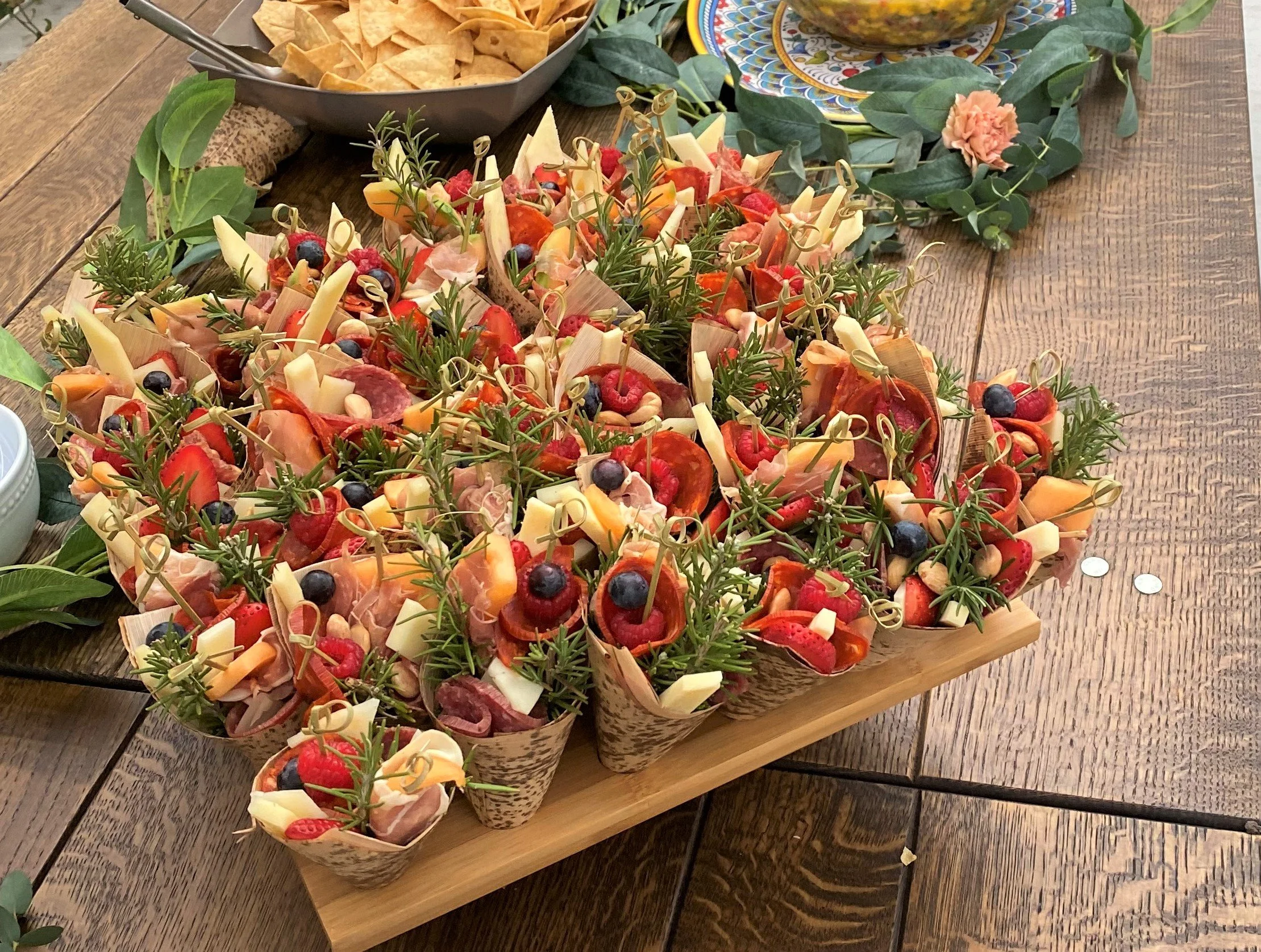 Artisanal charcuterie appetizer cones with cured meats, cheeses, fresh berries, and rosemary sprigs arranged on a wooden serving board for wedding cocktail hour catering.