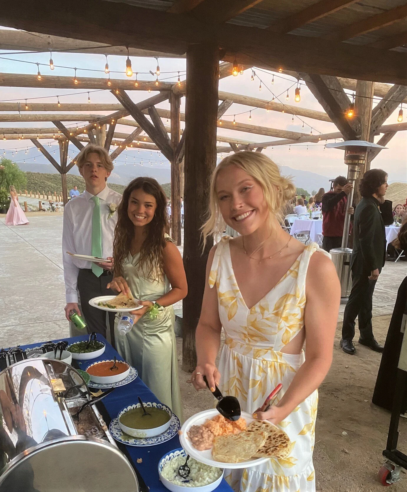 Joyful guests in formal attire enjoying a premium LaLa Tacos catering setup, featuring handmade quesadillas and fresh sides at an outdoor graduation celebration in Temecula.