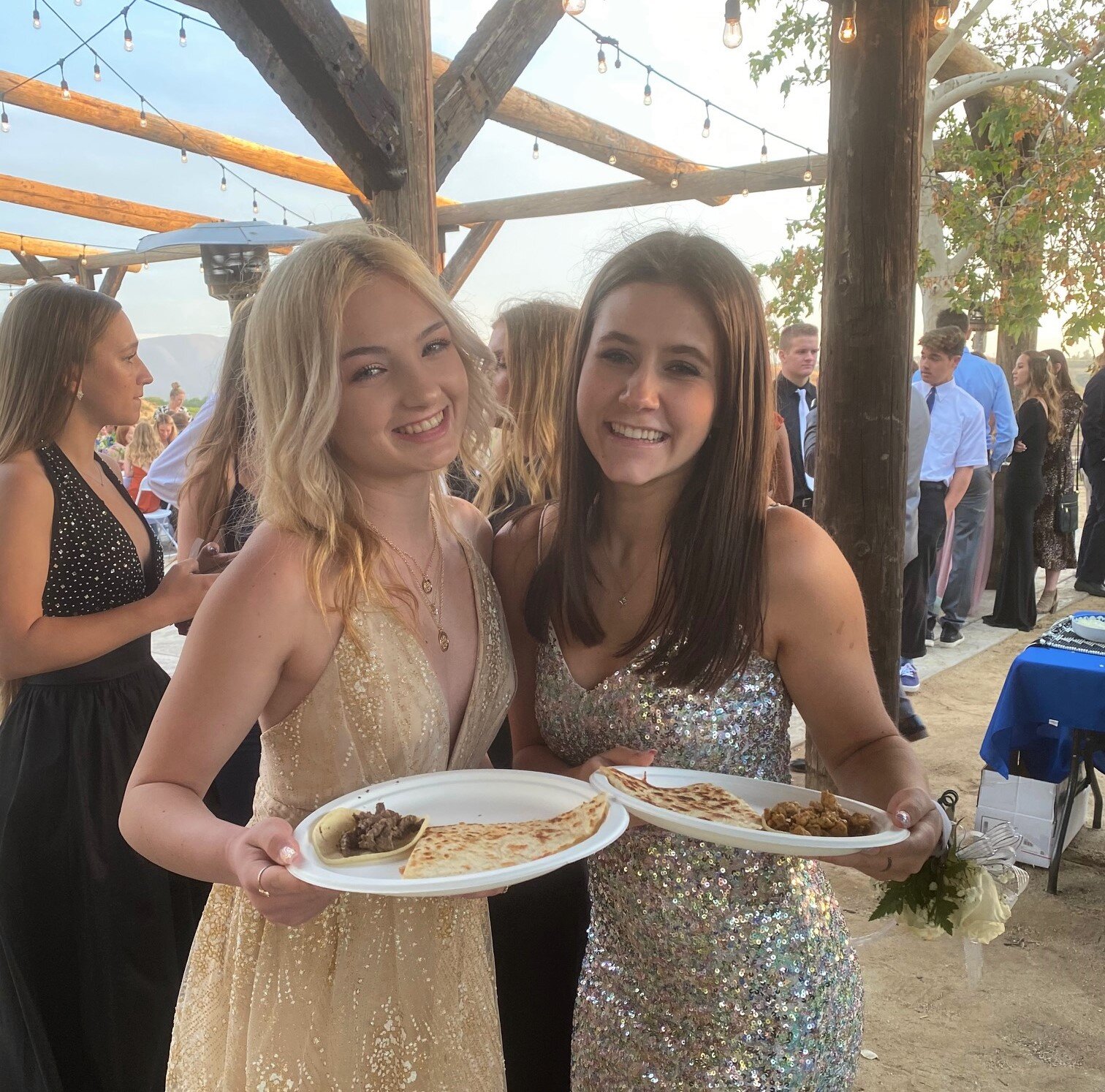 Two guests holding plates of tacos and quesadillas at a graduation catering event.