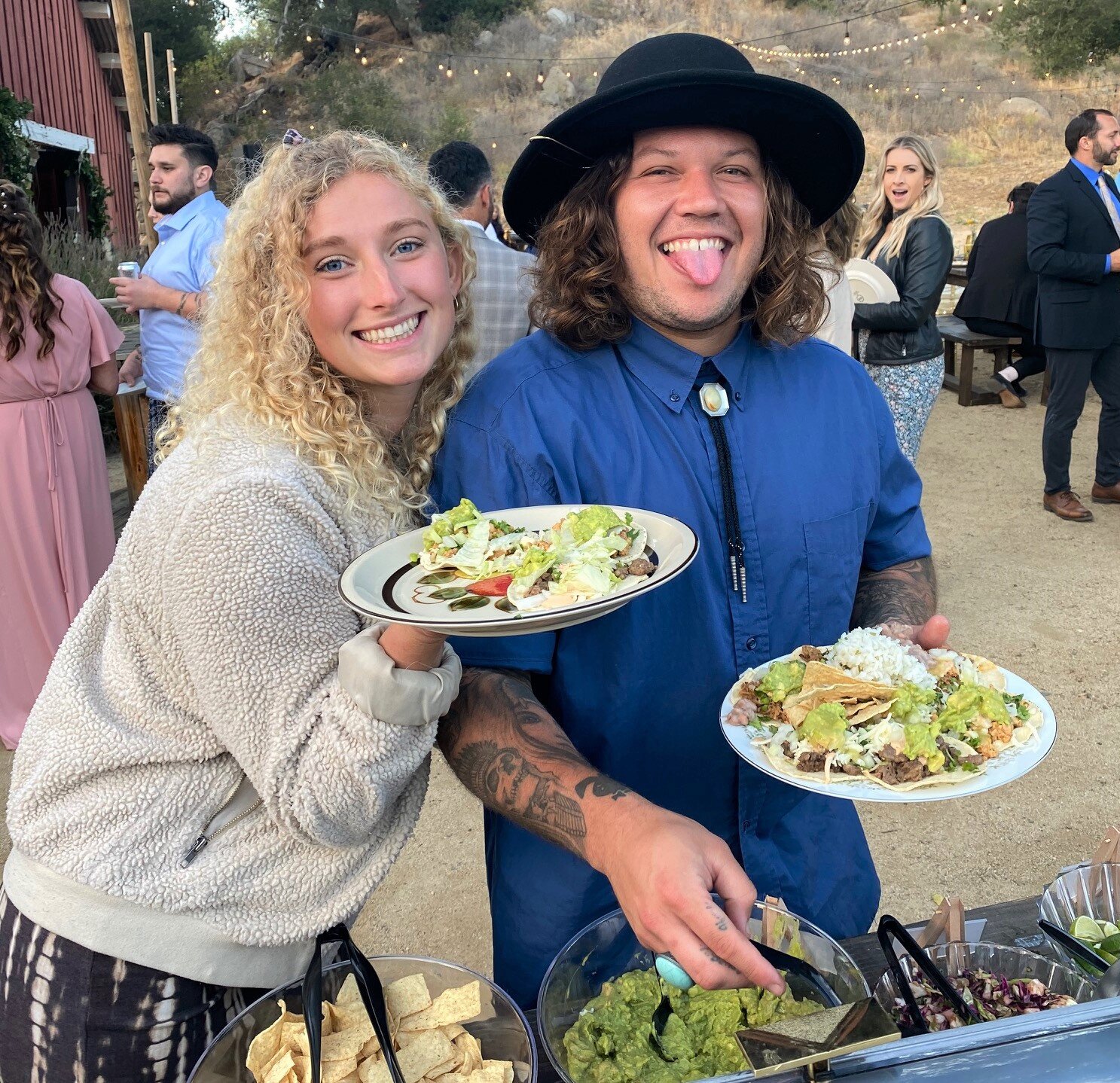 Guests posing with full plates of food at an outdoor wedding featuring mobile taco catering.