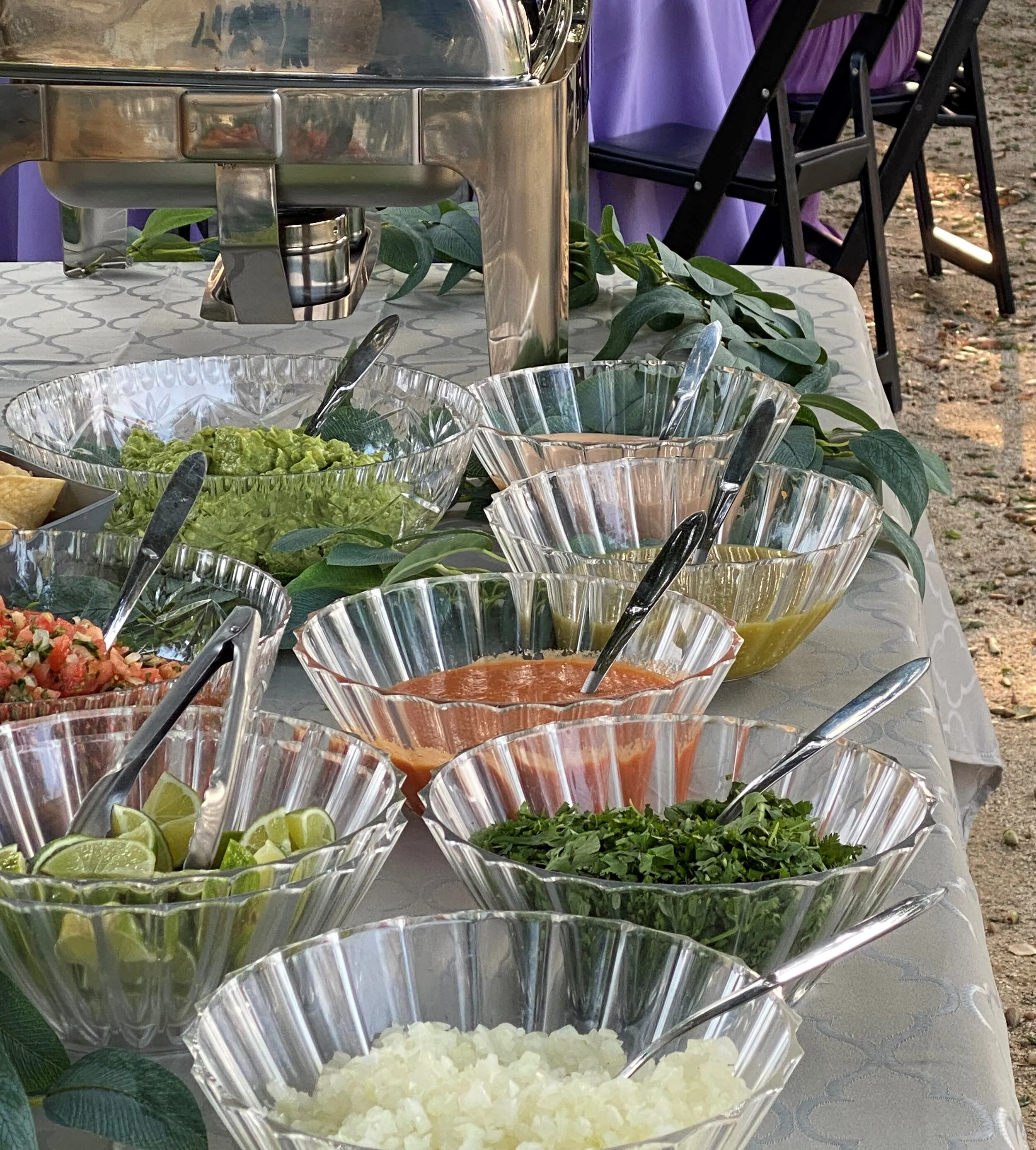 A freshly prepared salsa bar with guacamole, onions, cilantro, and limes for on-site taco catering.