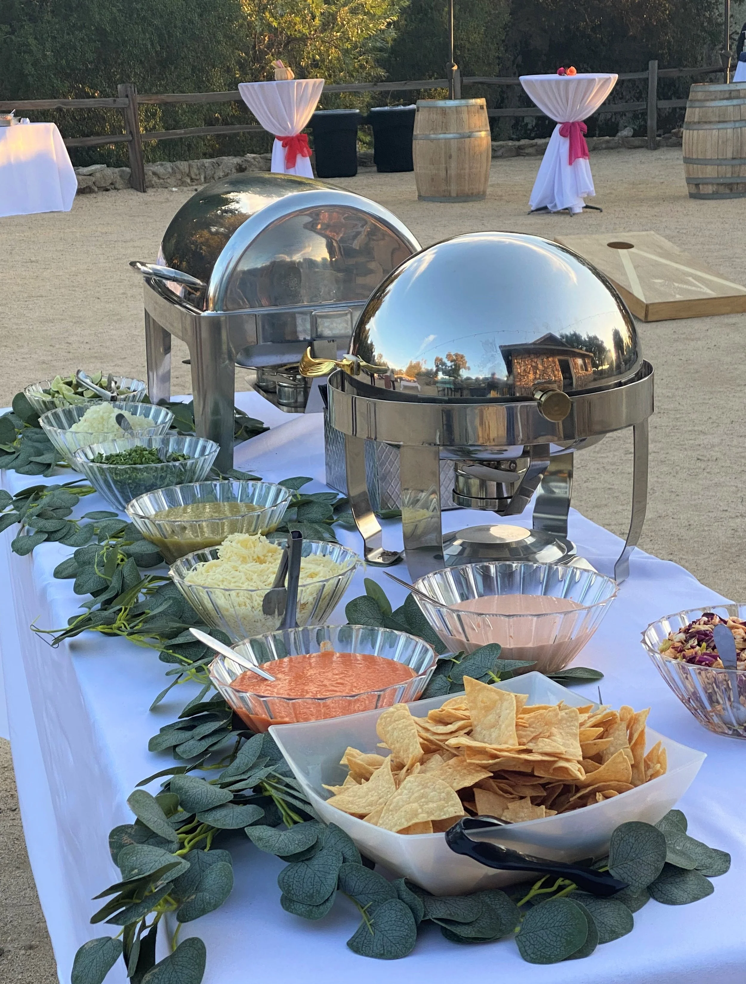 Premium outdoor wedding taco bar buffet setup with polished stainless steel chafing dishes glass salsa bowls and eucalyptus greenery decoration