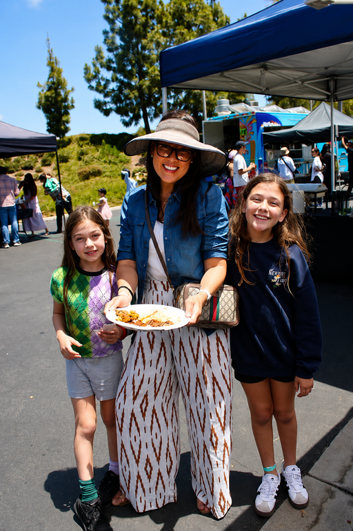 A mother and her two children holding plates of food during the LaLa Tacos & Churros taco bar at Rivian Family Day.