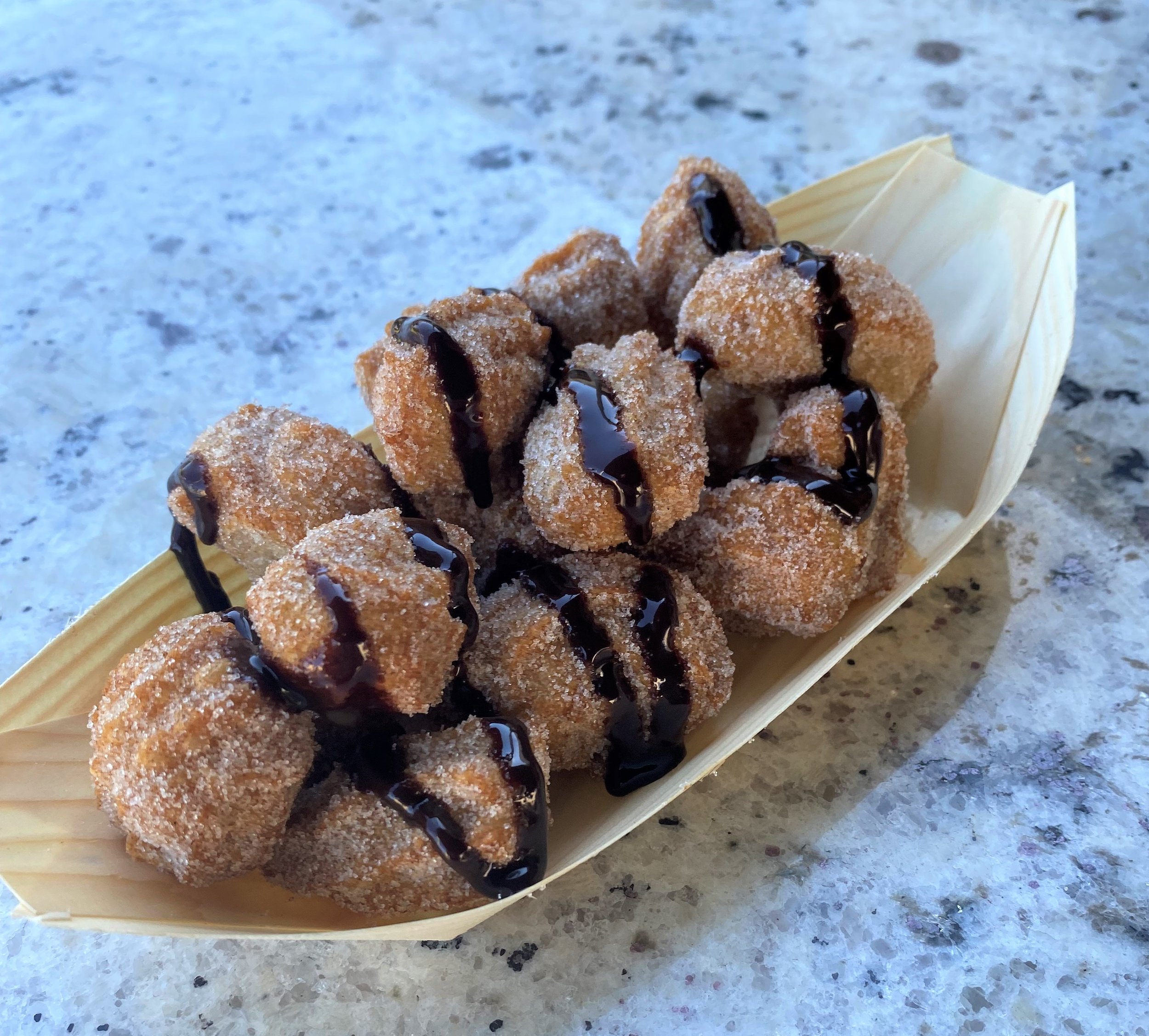 Freshly fried mini churros tossed in cinnamon sugar and drizzled with chocolate sauce served in a bamboo boat for event dessert catering
