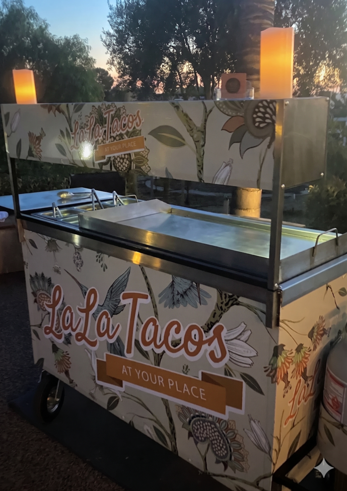 Custom-wrapped manned taco cart catering setup at a Coachella Valley event featuring authentic Mexican tacos cooked on-site, fresh toppings, homemade salsas, and professional taco cart service by LaLa Tacos.