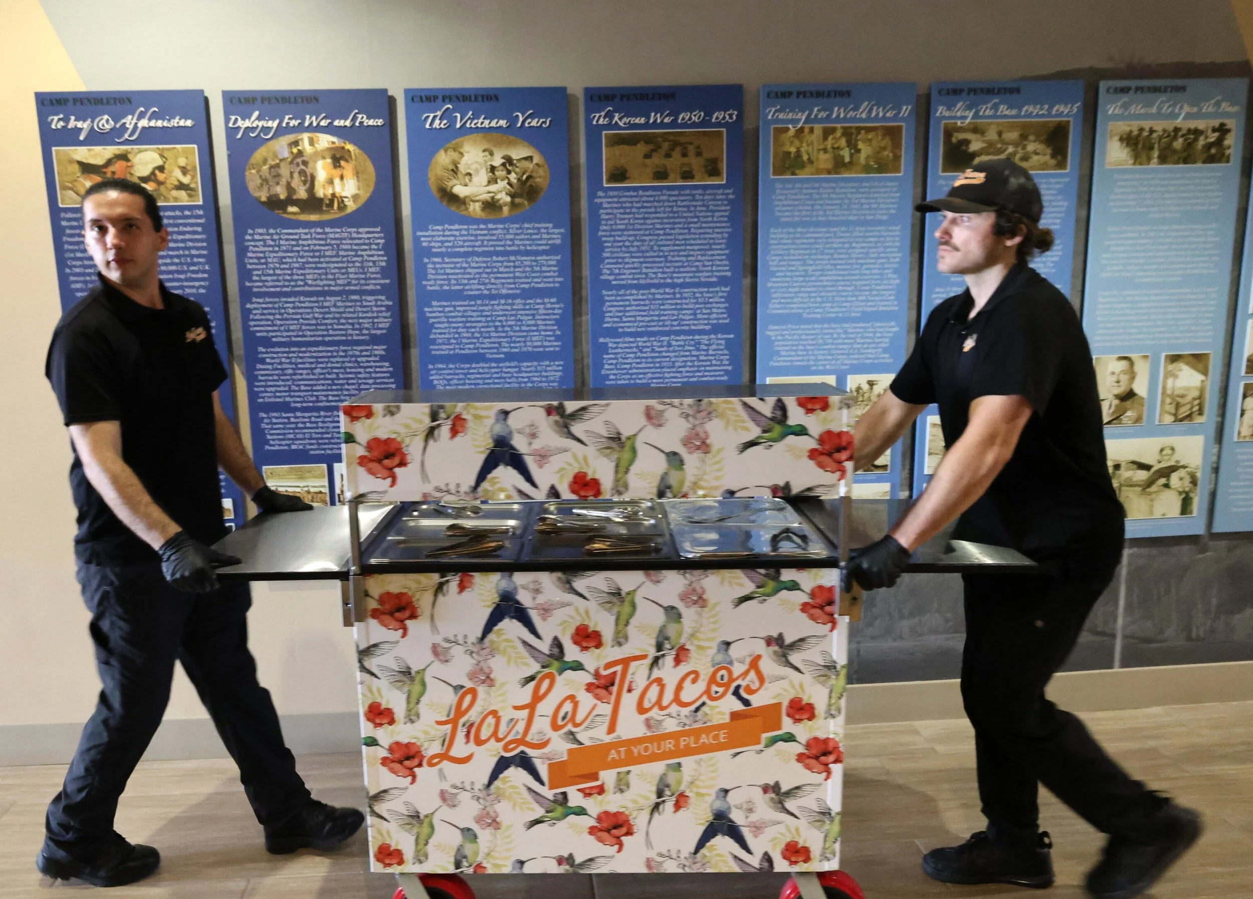 LaLa Tacos team positioning custom-wrapped taco catering cart in front of Camp Pendleton historical displays for a formal military event.