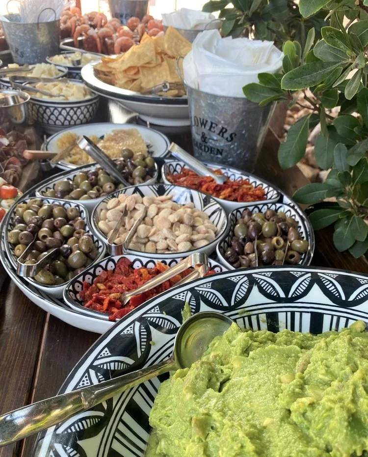 Upscale charcuterie grazing table featuring fresh guacamole, gourmet olives, sun-dried tomatoes, and premium appetizers in patterned ceramic dishes