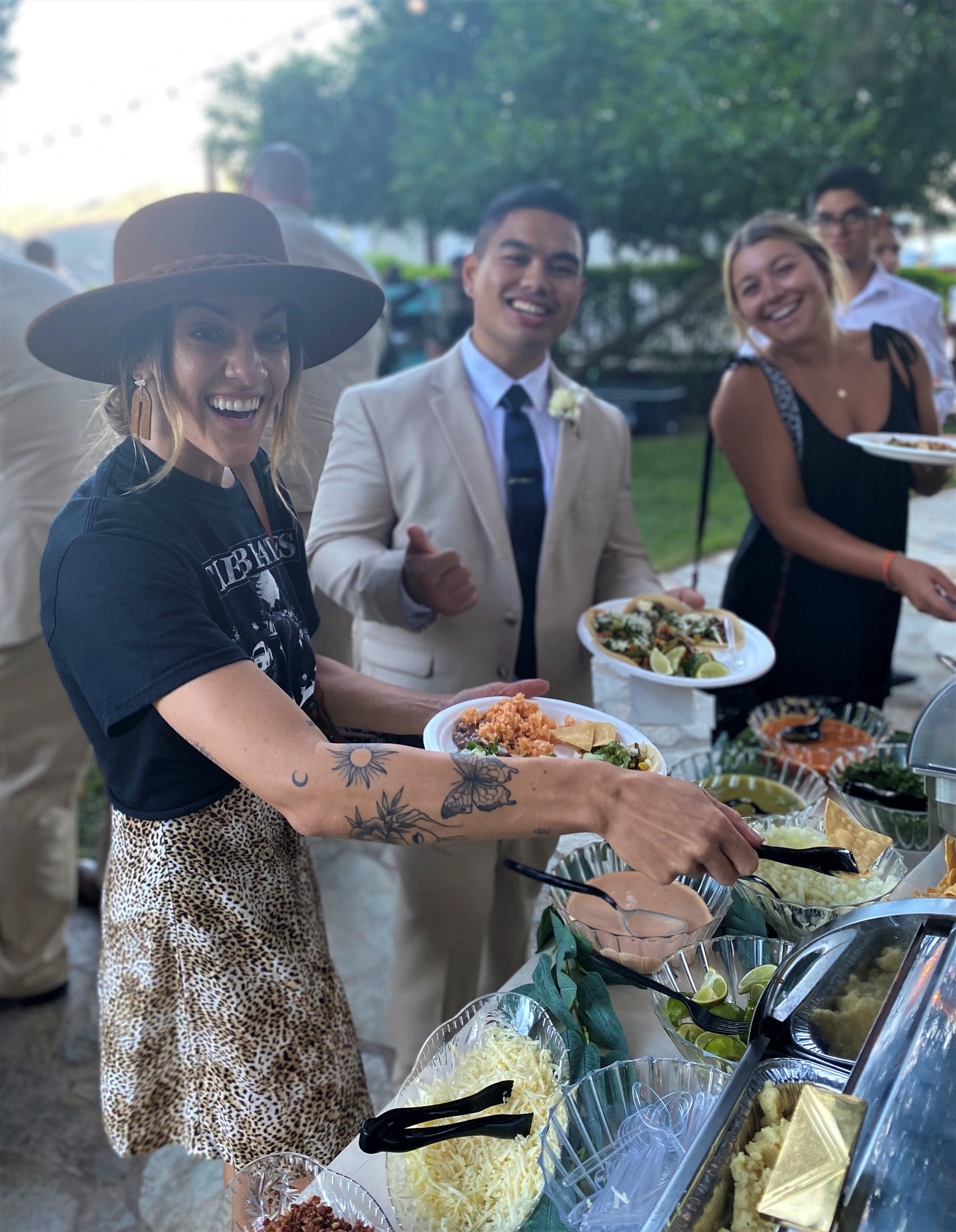 Joyful wedding guests in formal attire serving themselves from an elegant artisan taco bar, featuring fresh toppings in crystal-cut bowls, catered by LaLa Tacos at Secluded Garden in Temecula.