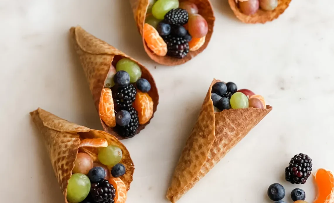 Artisan seasonal fruit cones with fresh berries, grapes, and citrus, presented in sustainable bamboo cones for boutique event catering