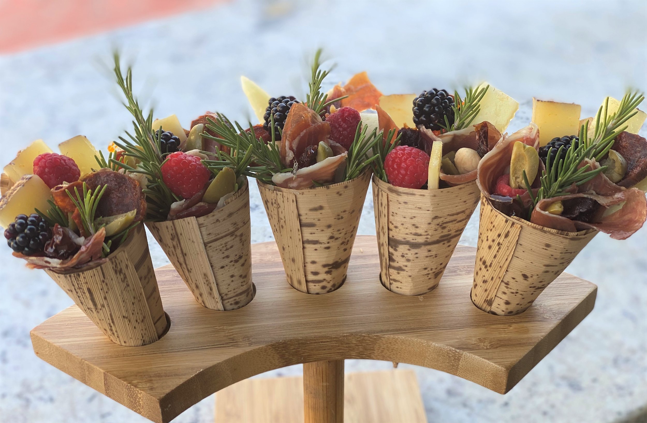 Elegant individual charcuterie cones displayed in a custom wooden stand, filled with premium cured meats, artisan cheeses, fresh berries, and rosemary sprigs for a luxury catered event by LaLa Tacos.