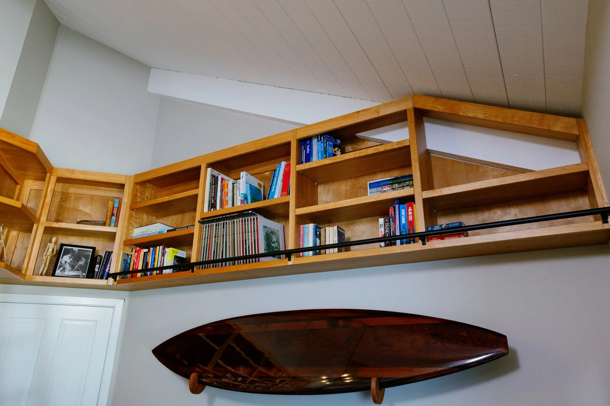 A wooden bookshelf filled with books and photographs, located above a dark polished wooden table in a room with white walls and a sliding door.