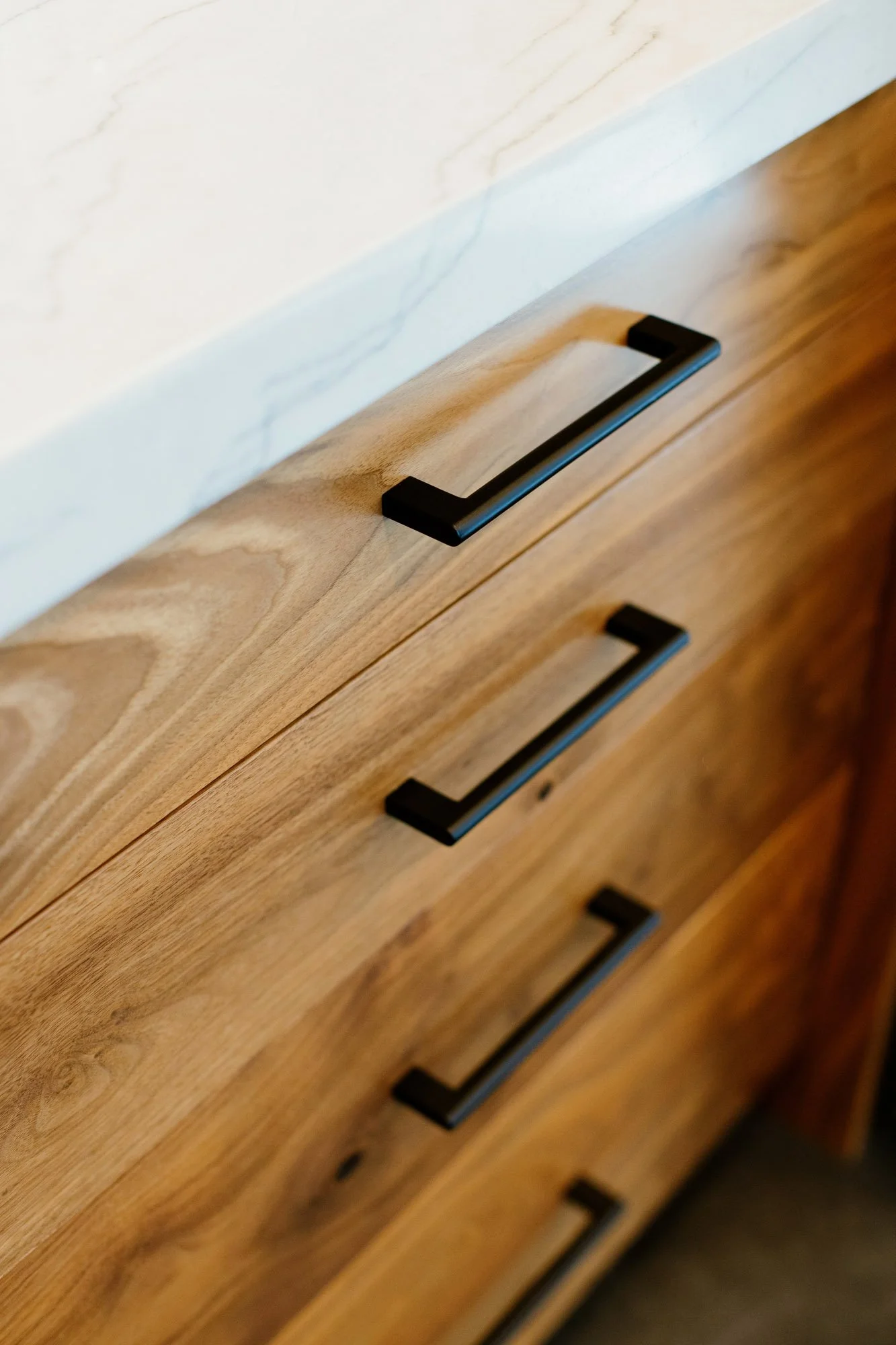 Close-up photo of a wooden dresser with black metal handles and a white marble countertop.