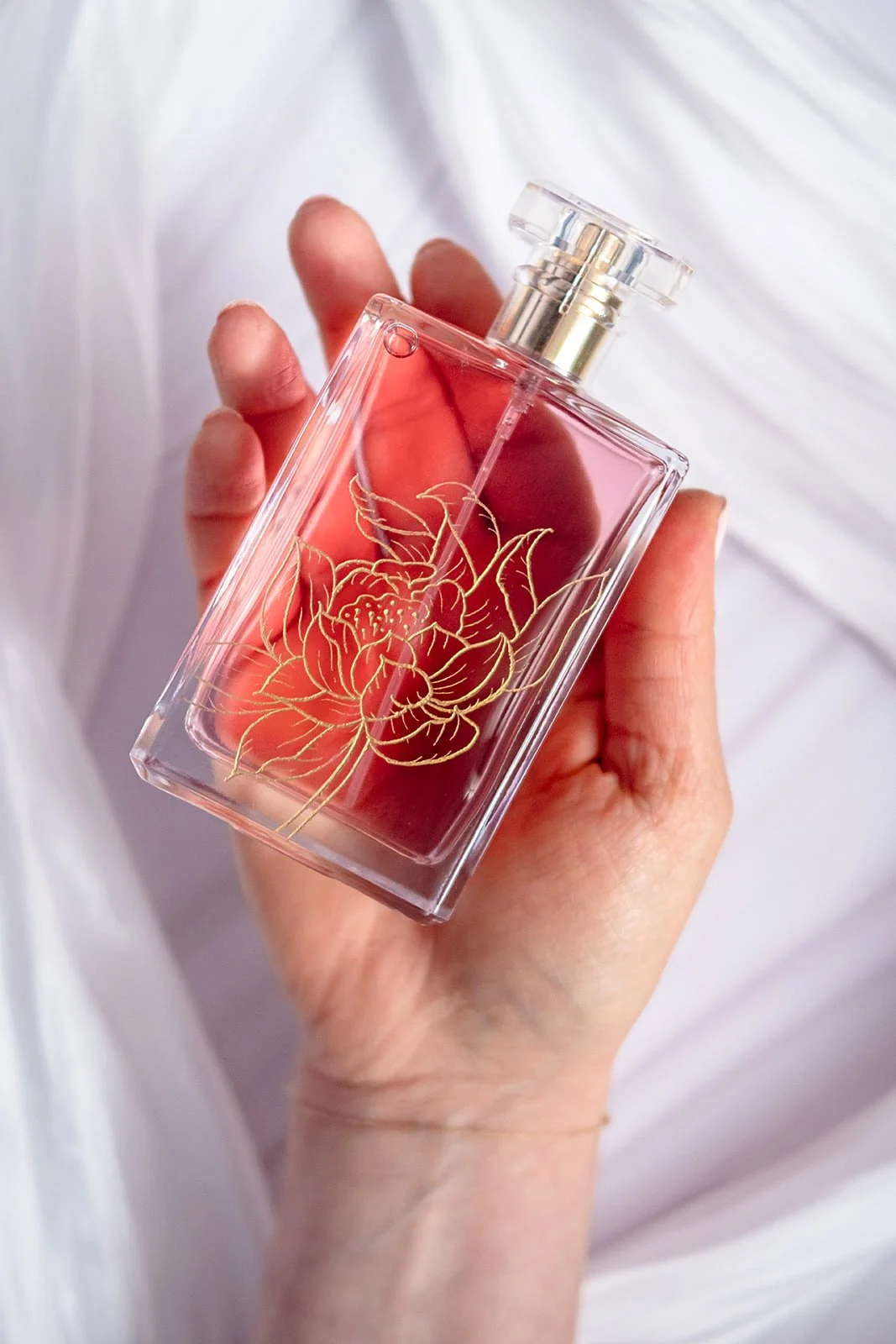 A hand holding a perfume bottle with an intricate peony engraving