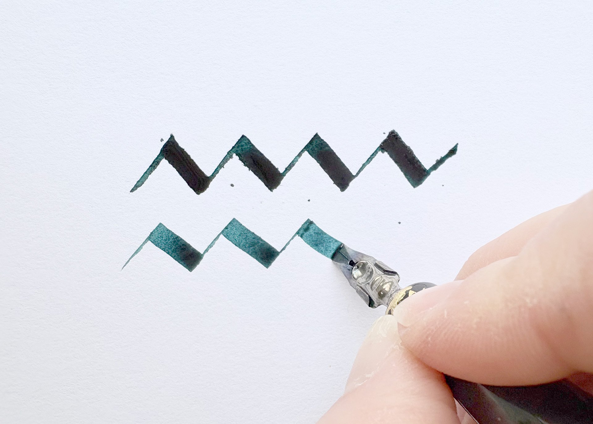 A close up showing a hand writing a thick line using a broad nib pen