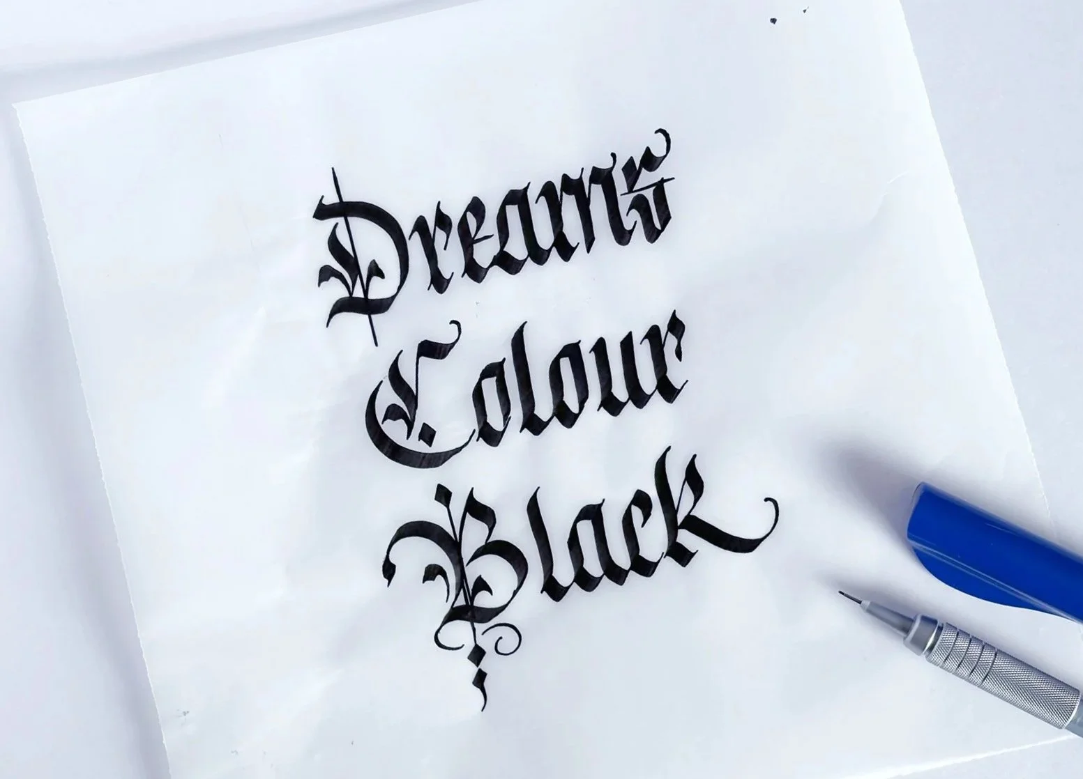 The words Dreams Colour Black written in blackletter calligraphy. Mechanical pencil and pilot pen cropped off bottom right corner.
