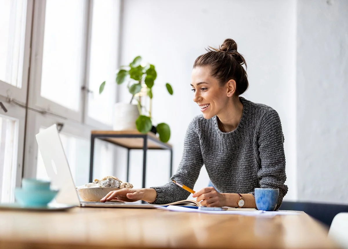 a smiling woman looking at her laptop in a home setting.